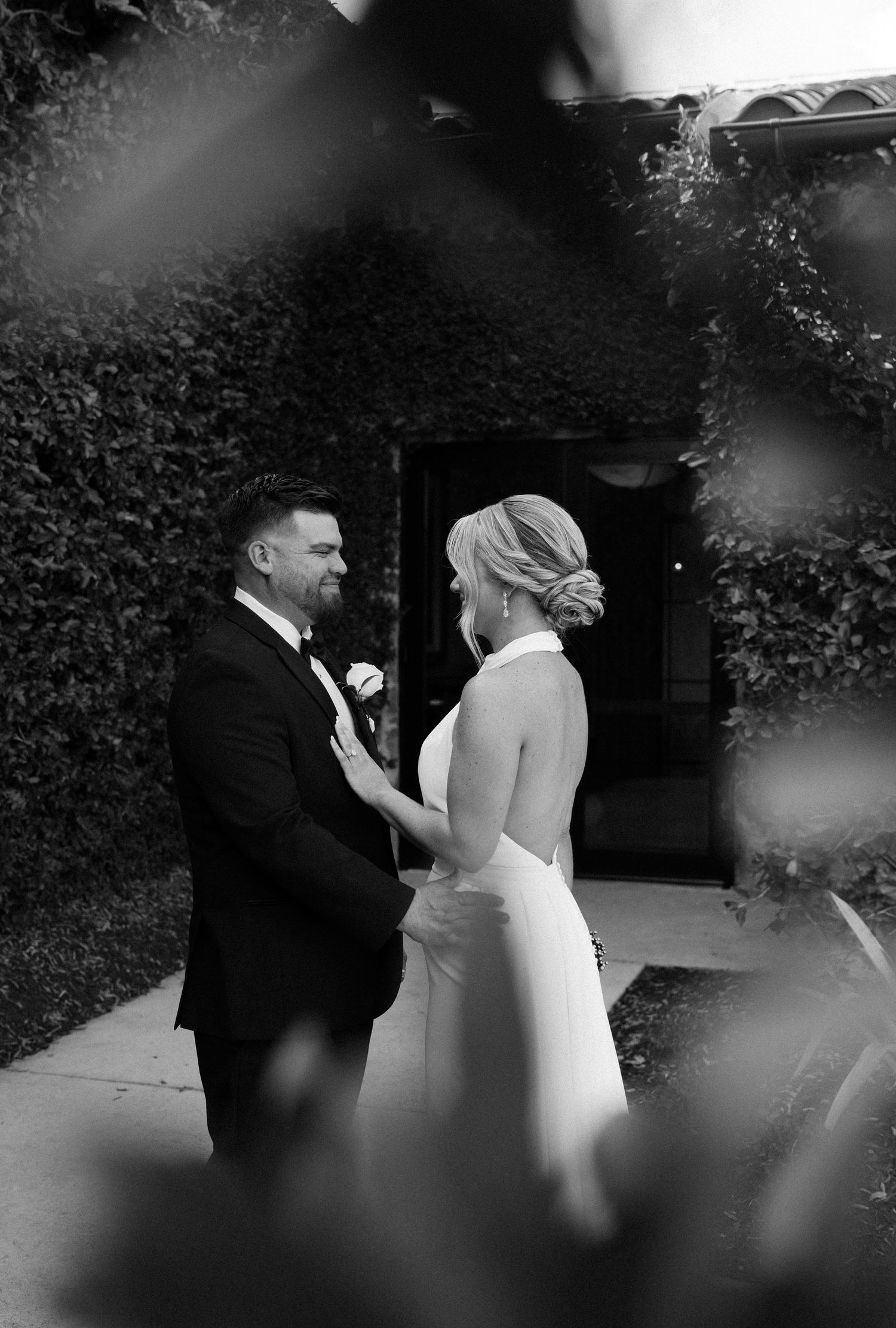 Black and white image of couple sharing an intimate wedding moment against an ivy-covered wall.