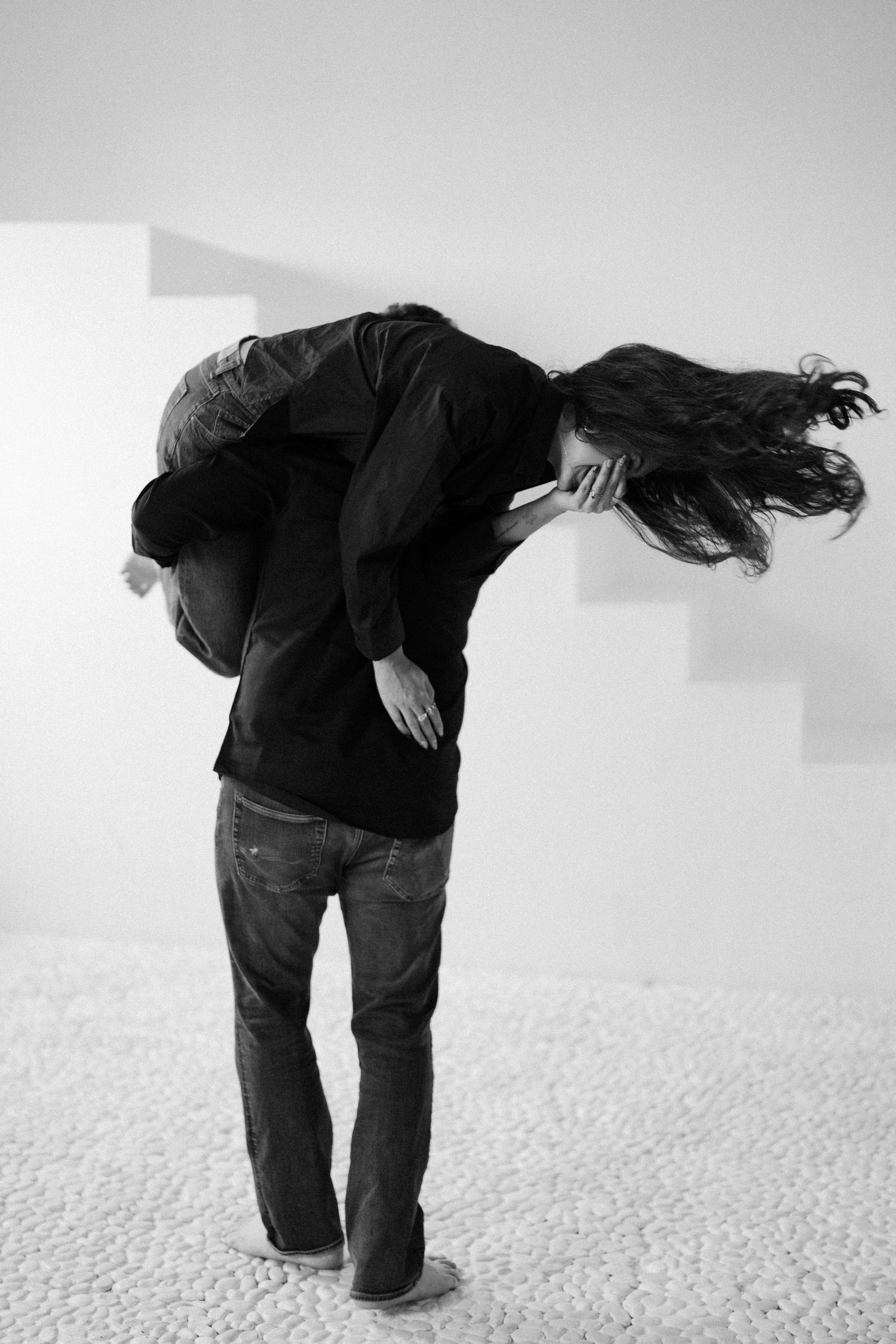 A black and white photograph shows a person bending forward with long dark hair flowing dramatically to one side.