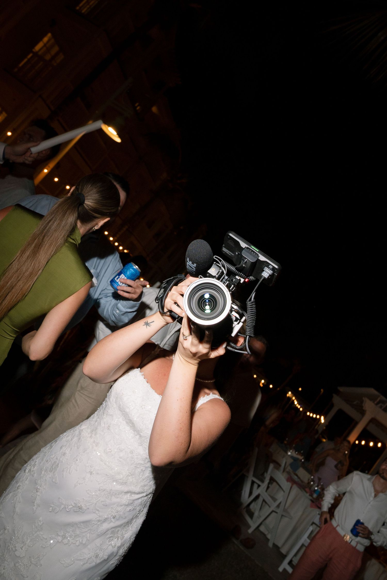 Wedding guest in white dress taking photos with a professional camera at night.