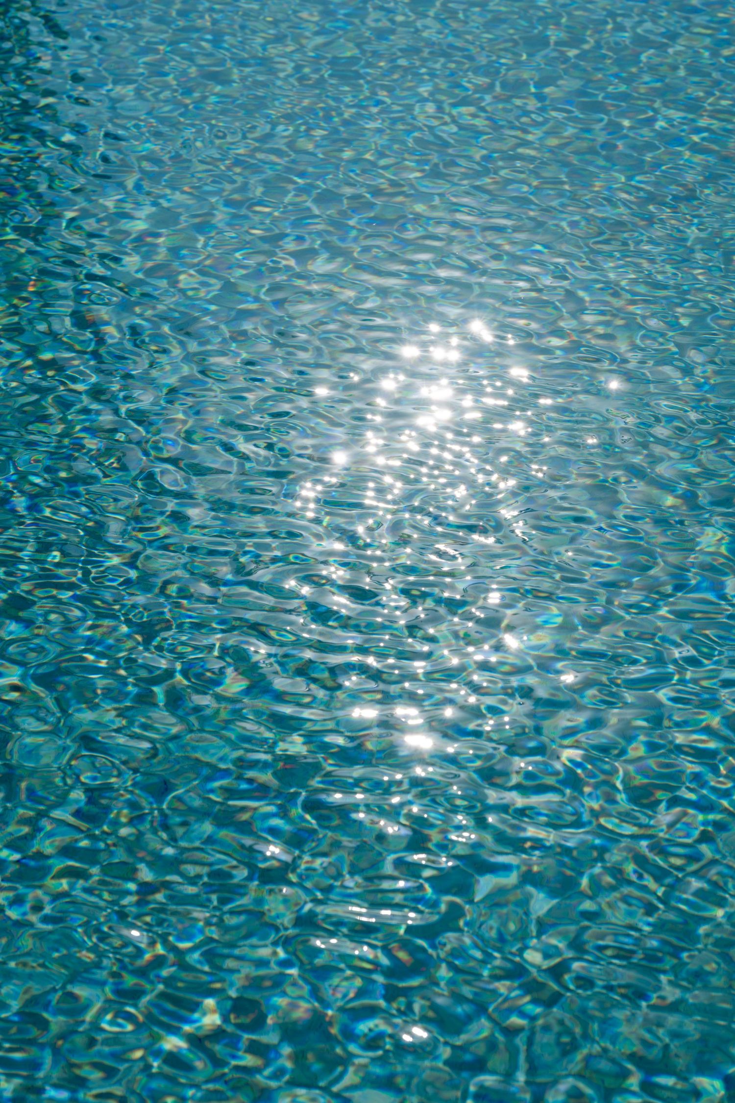 Rippling turquoise swimming pool water with sunlight reflections creating a mesmerizing pattern.