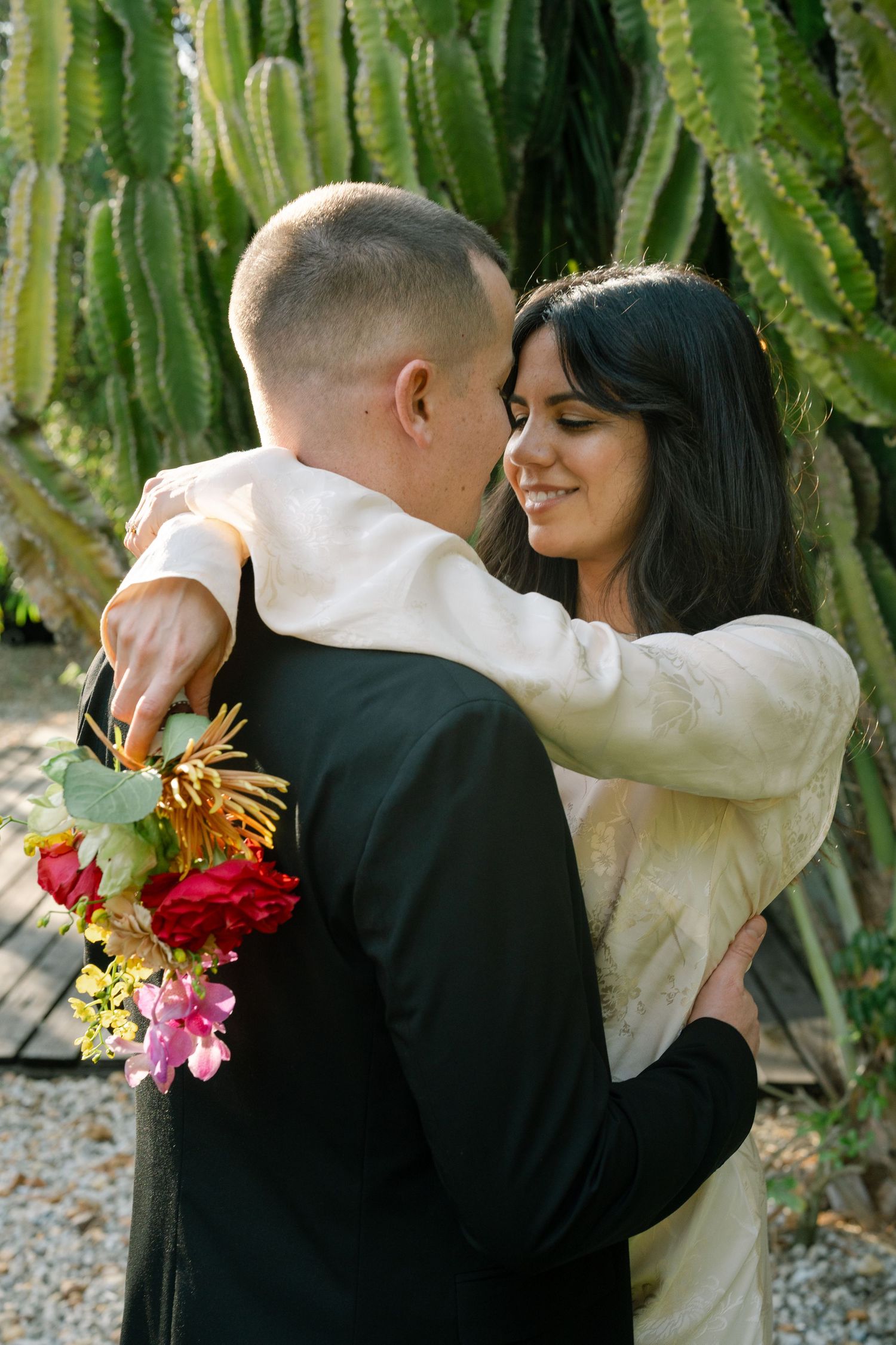 Wedding couple embracing with colorful bouquet against cactus garden backdrop.