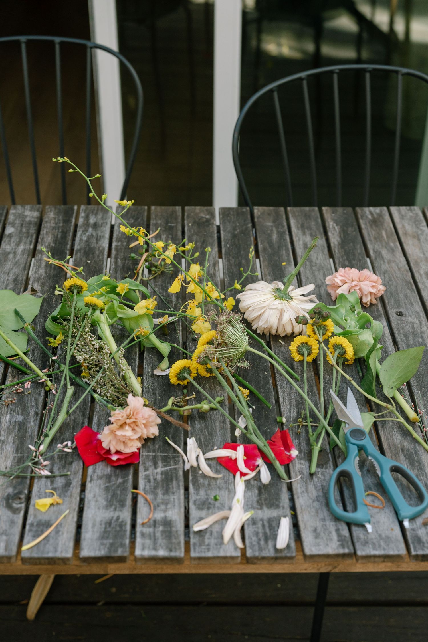 Fresh cut flowers and gardening tools arranged on a rustic wooden table with chairs.