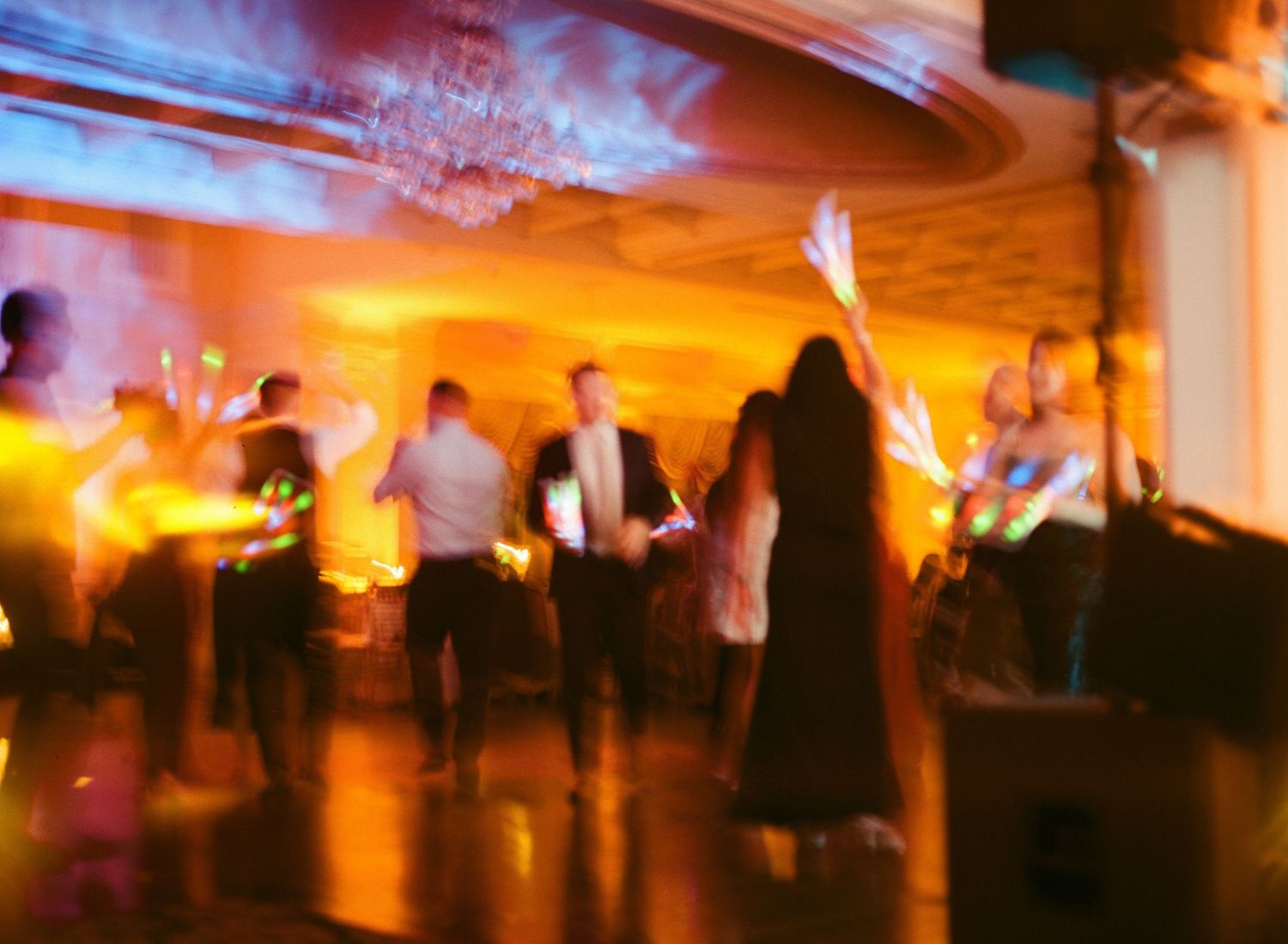 Blurred motion of people dancing at an evening event with warm orange lighting and elegant decor.