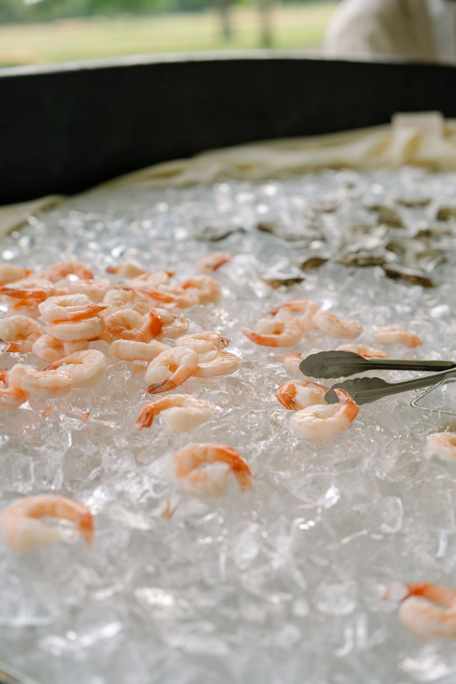 Fresh shrimp cocktail served on a bed of crushed ice with silver tongs at an outdoor catered event.