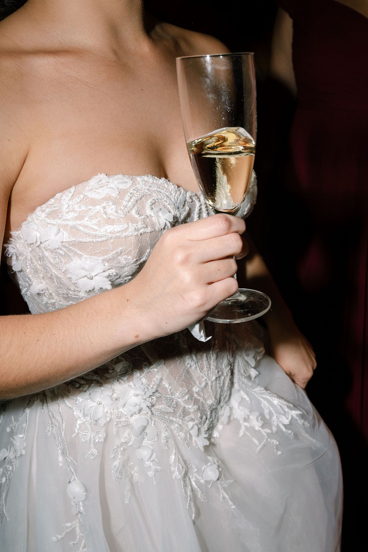 Bride in a lace off-shoulder gown holding a champagne flute at her wedding reception.