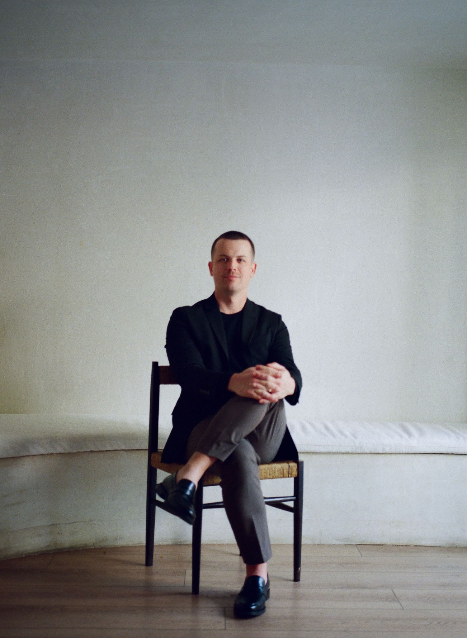 Minimalist portrait sequence showing a person seated on a dark chair against a white wall.