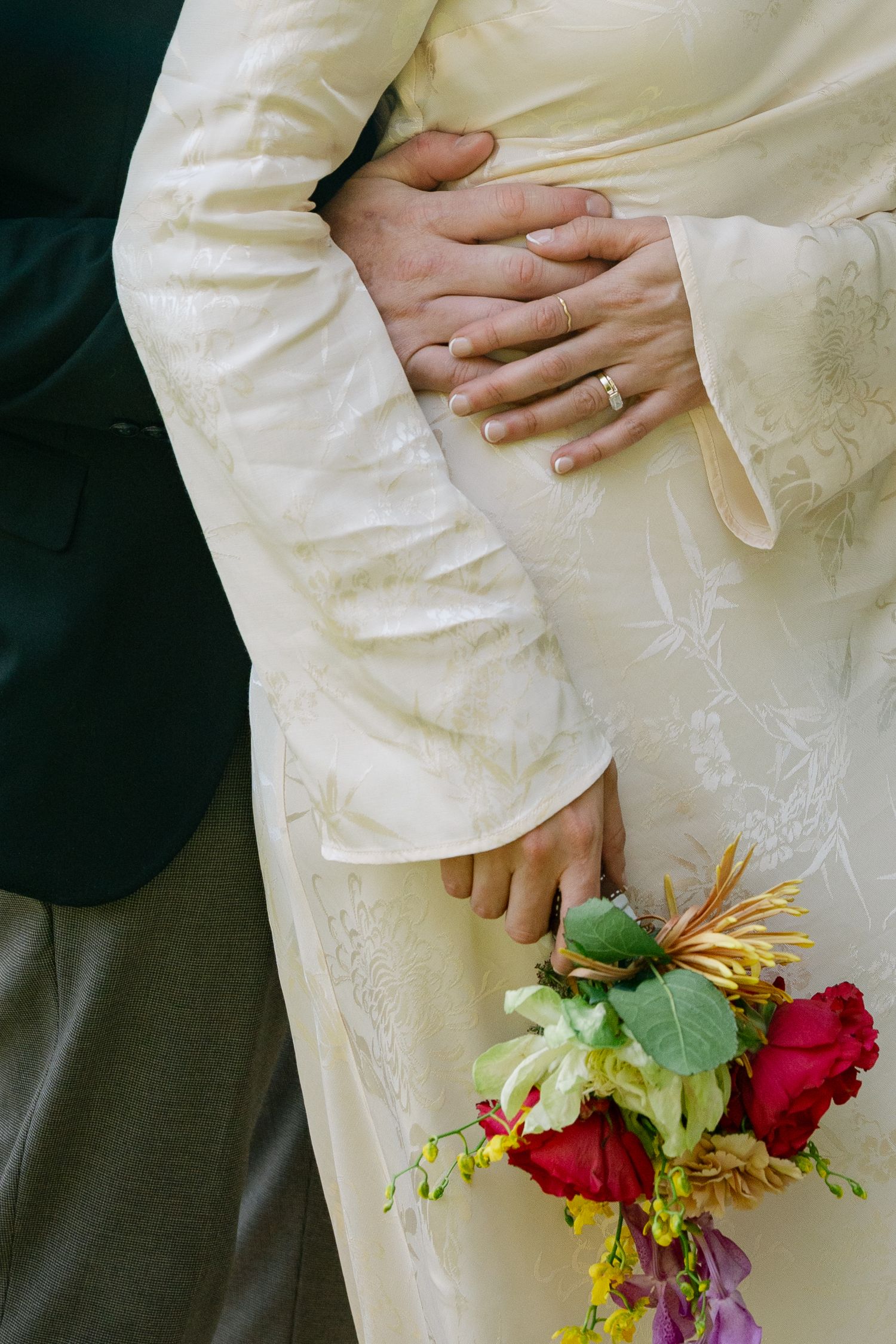 Close-up of hands holding colorful flowers against white fabric with delicate embroidery.