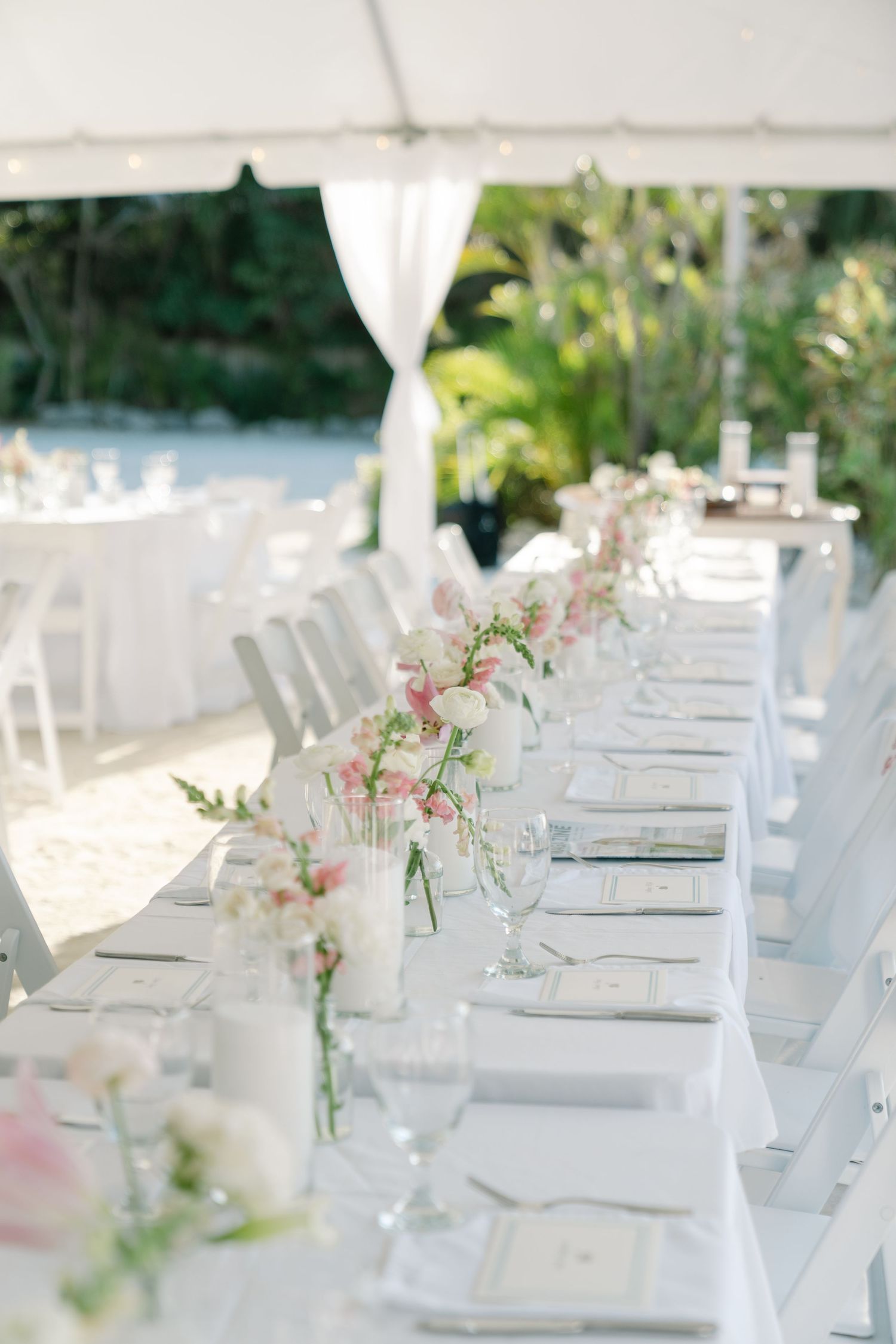 A long table set for an outdoor event or wedding, with floral arrangements and place settings along the length of the table.