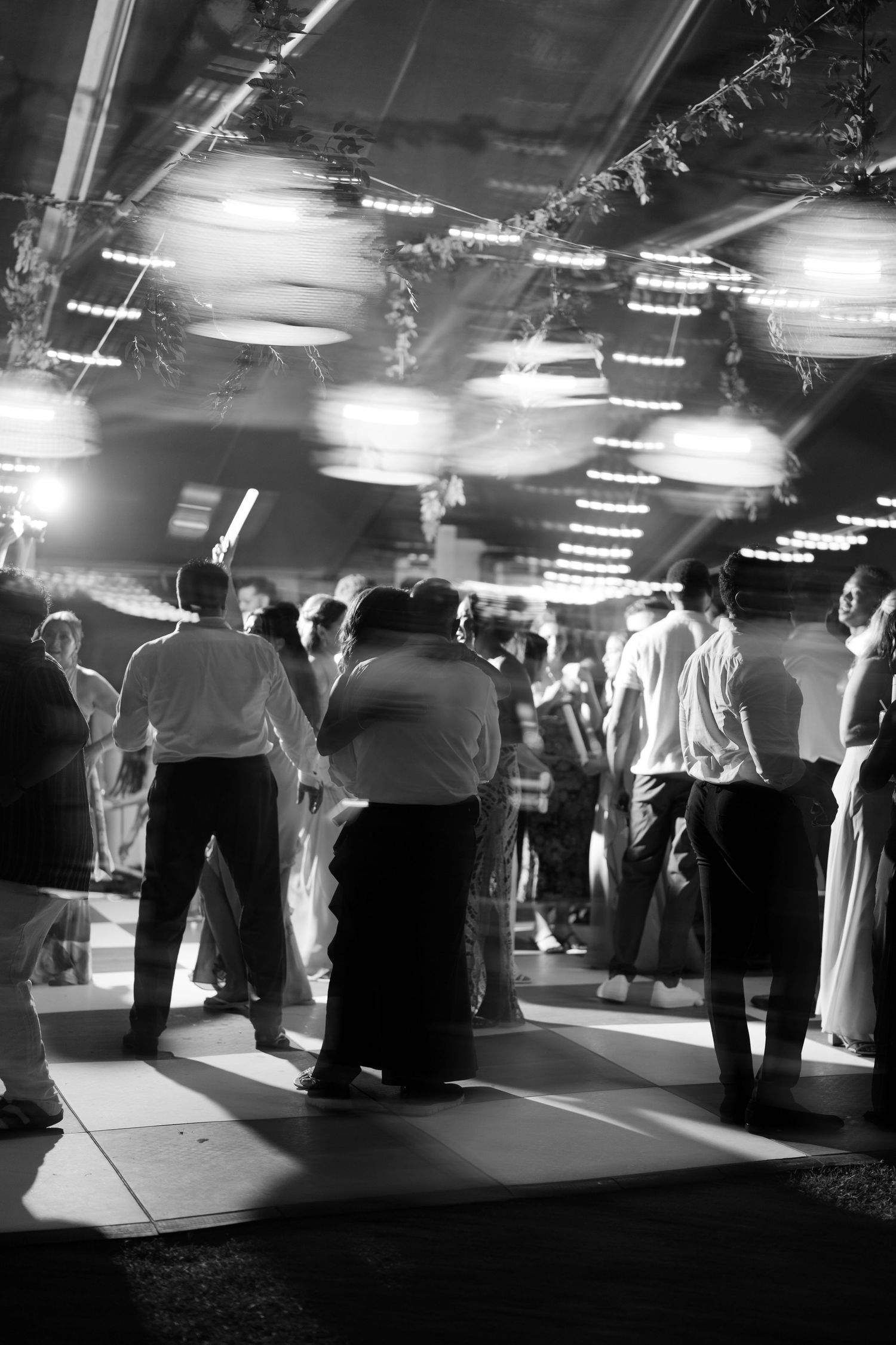 Wedding reception guests dancing under glowing lights in a lively black and white celebration photo.