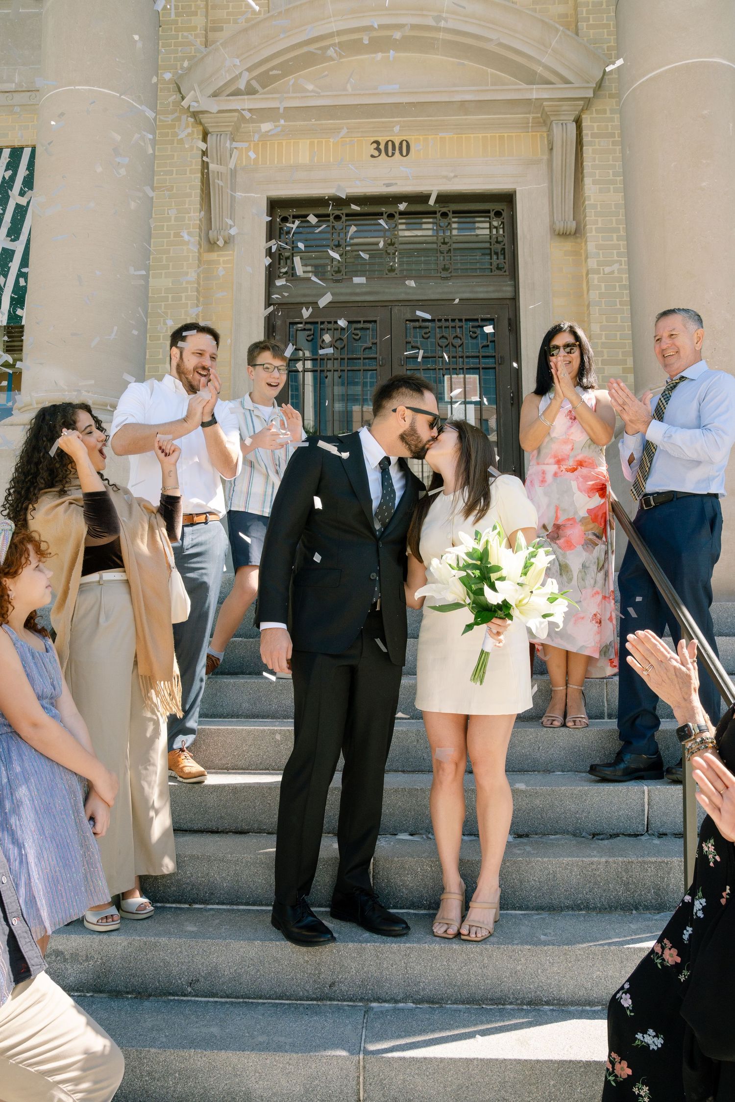 Wedding party members dance and celebrate together outside a historic building with ornate architecture.