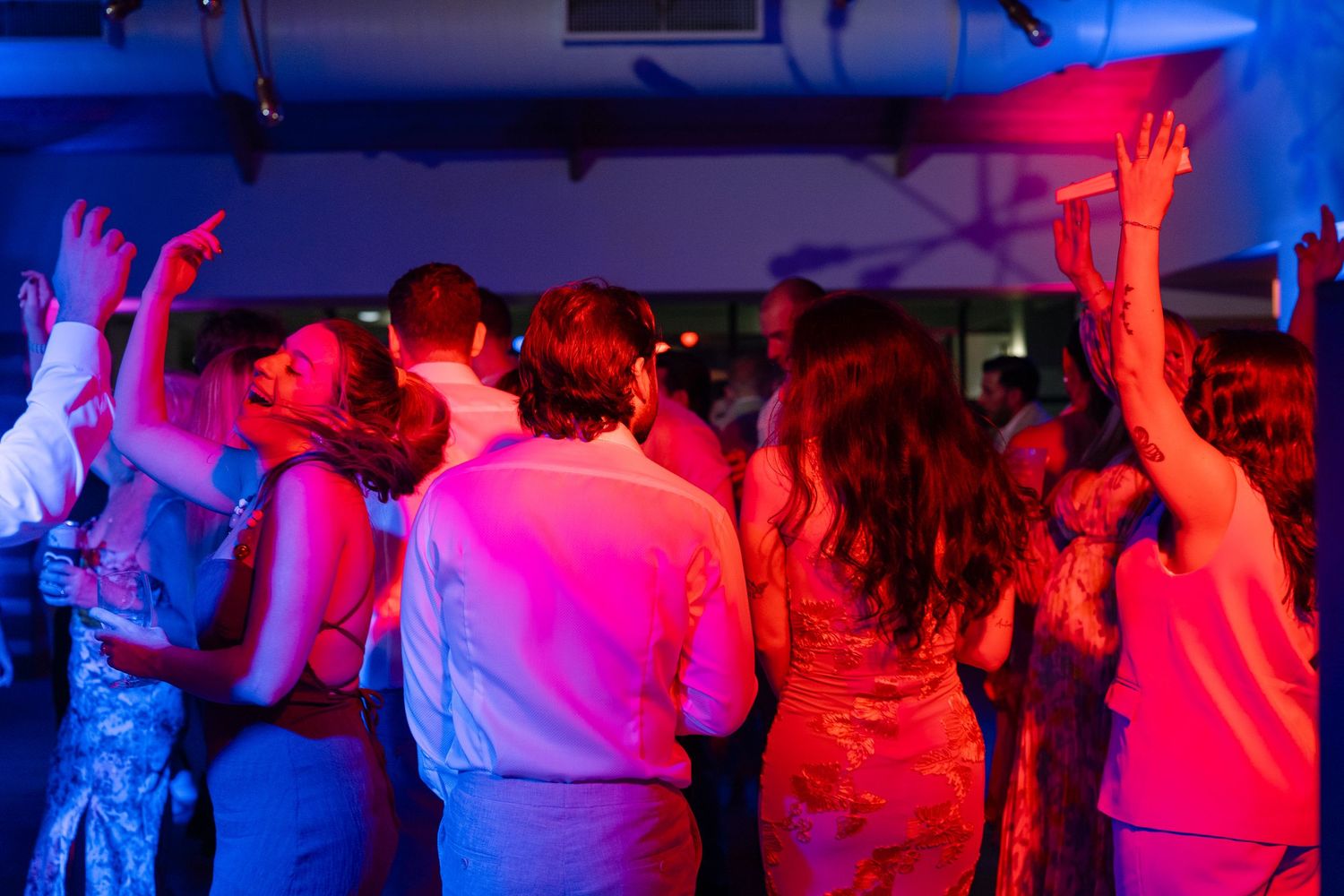 Wedding guests dance under colorful red and blue lighting at a reception party.