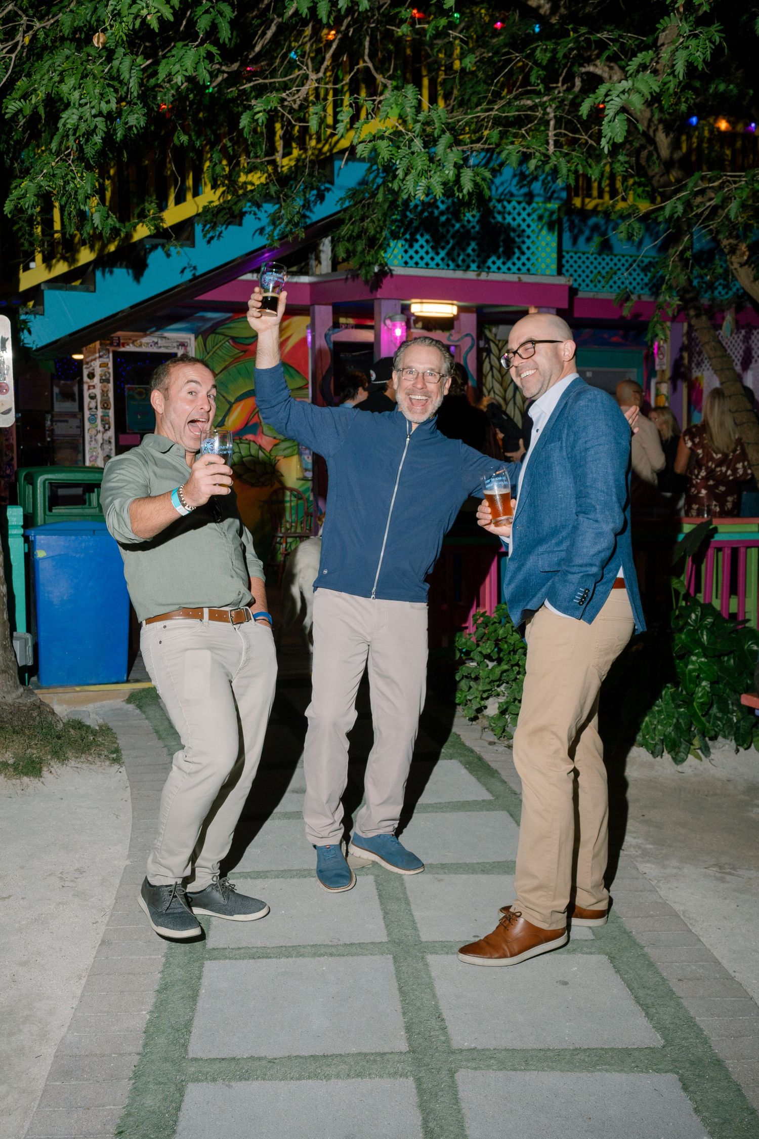 A sequence of people jumping and dancing in a line at an outdoor nighttime event.