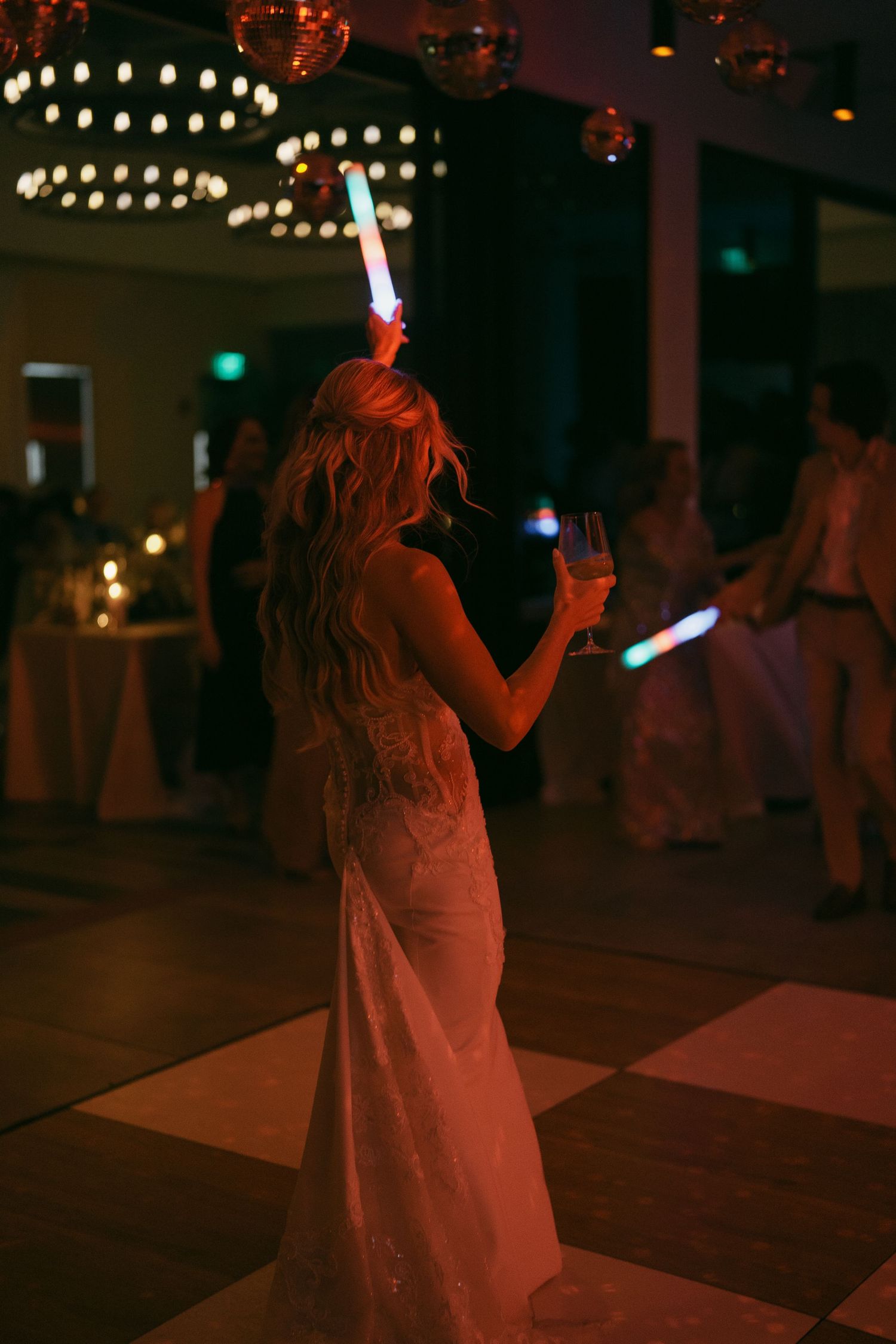 People dancing with glowing light sticks under string lights at a nighttime celebration.