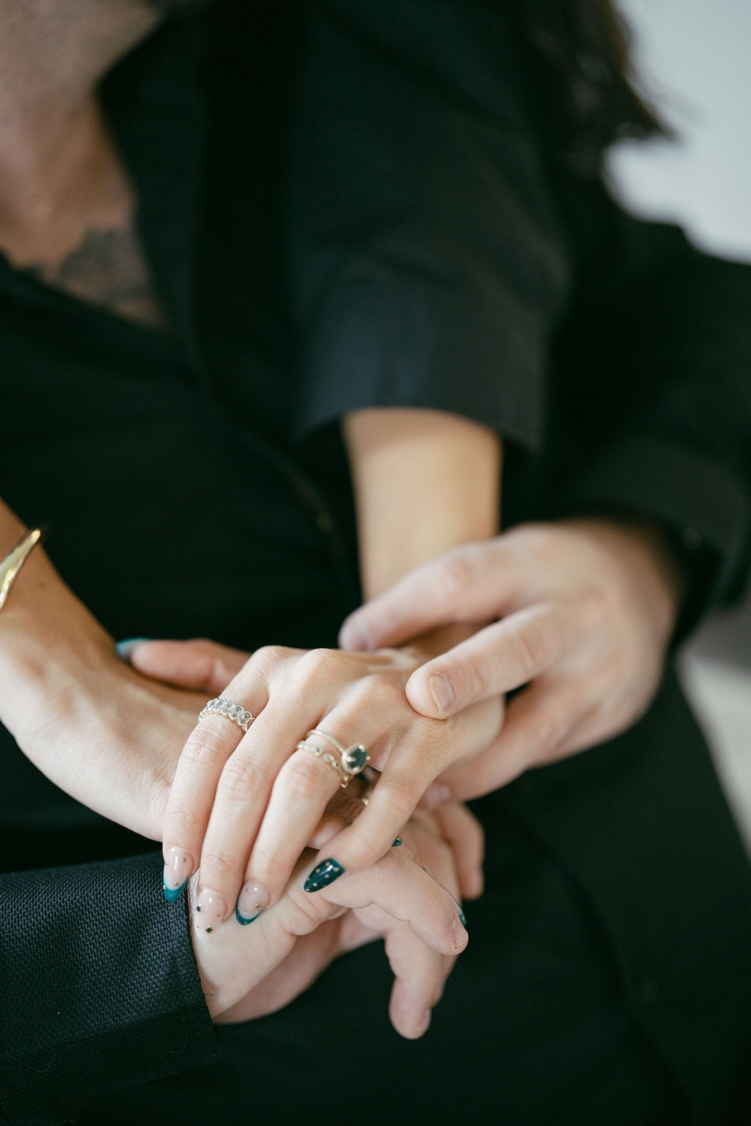 Close-up view of hands wearing turquoise rings and nail polish with black clothing in soft lighting.