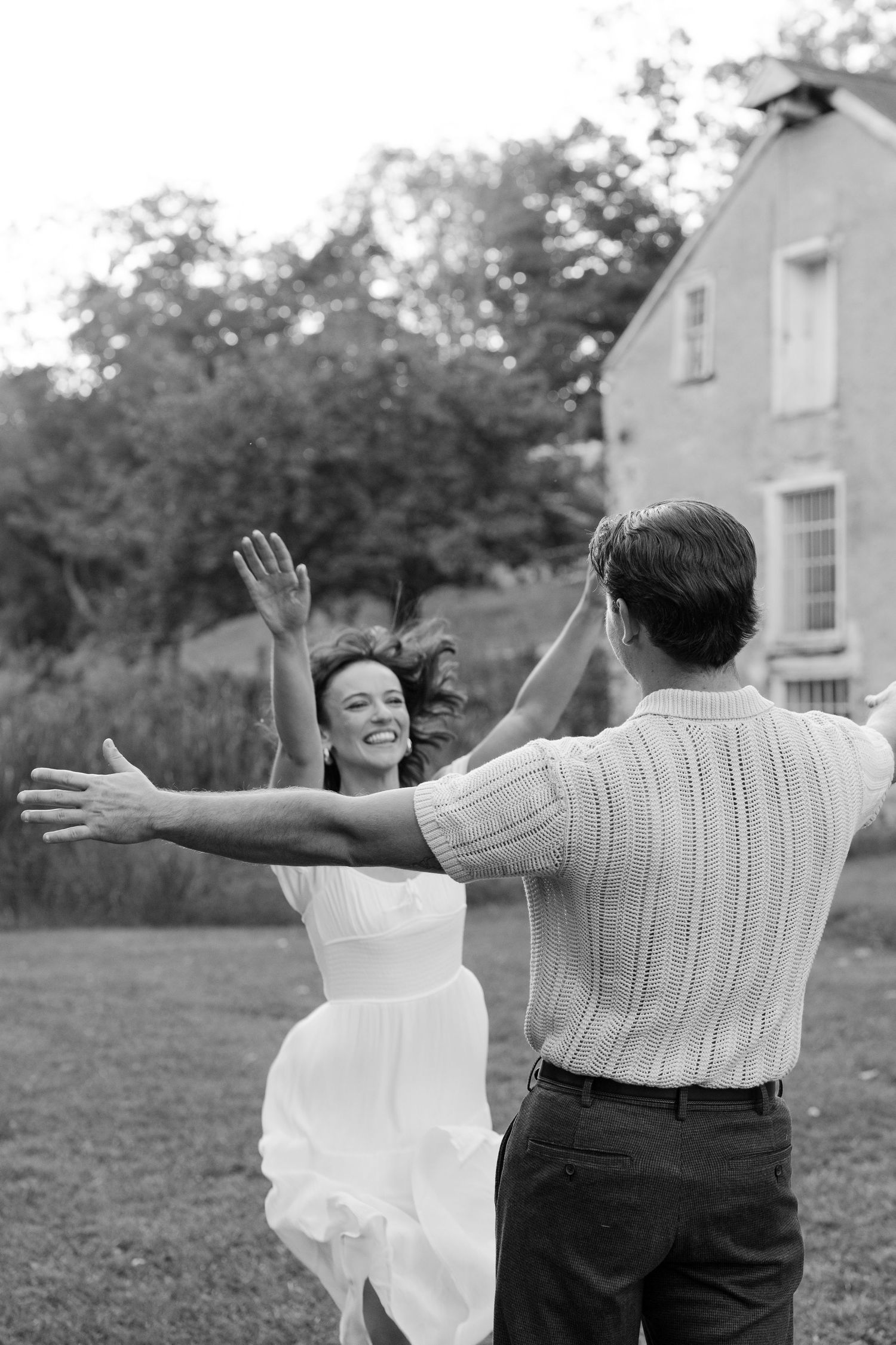 Joyful couple dancing outdoors in black and white photo near historic stone building.
