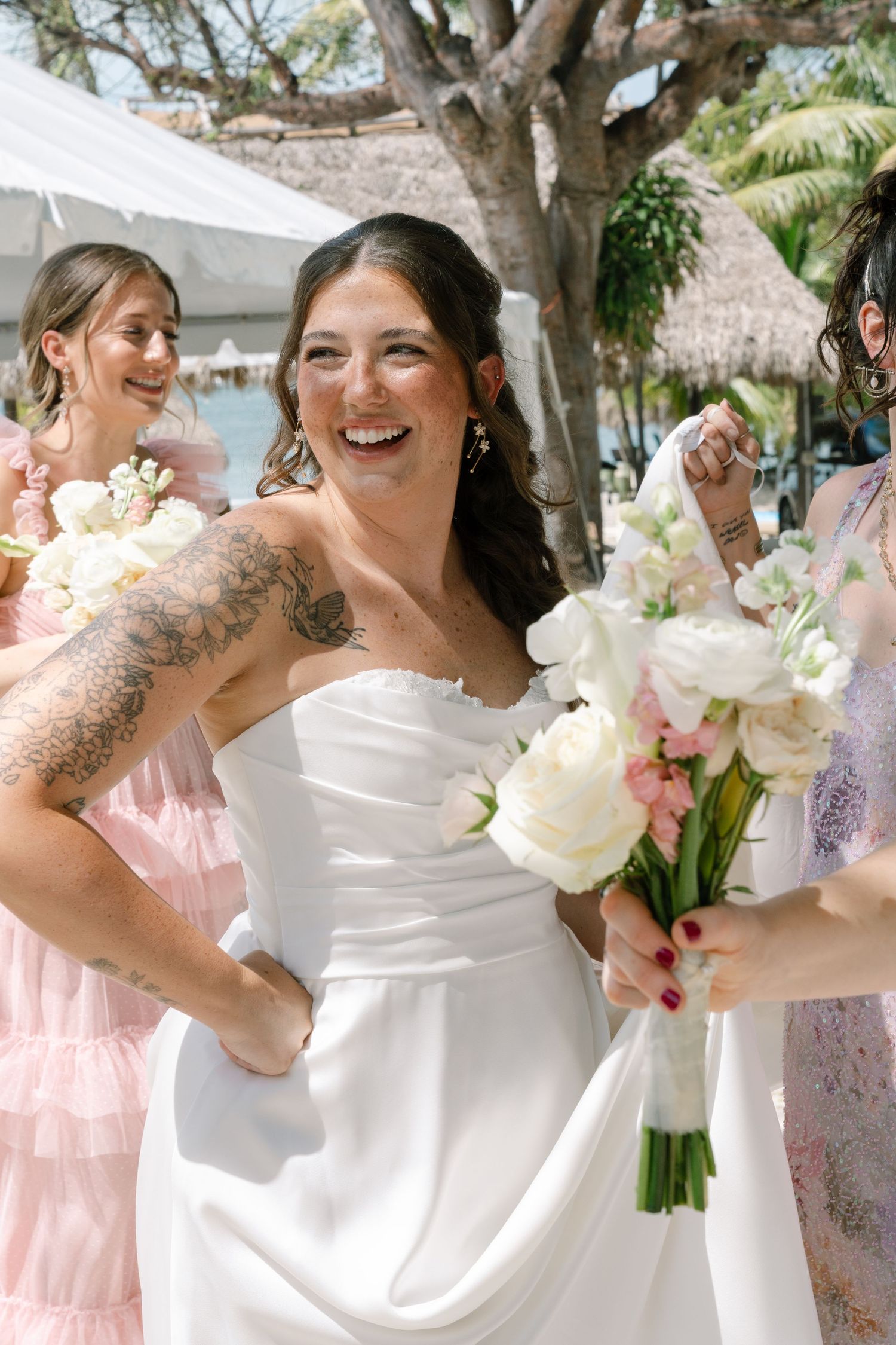 A bride and her bridesmaids are laughing and holding bouquets of flowers in a garden setting.