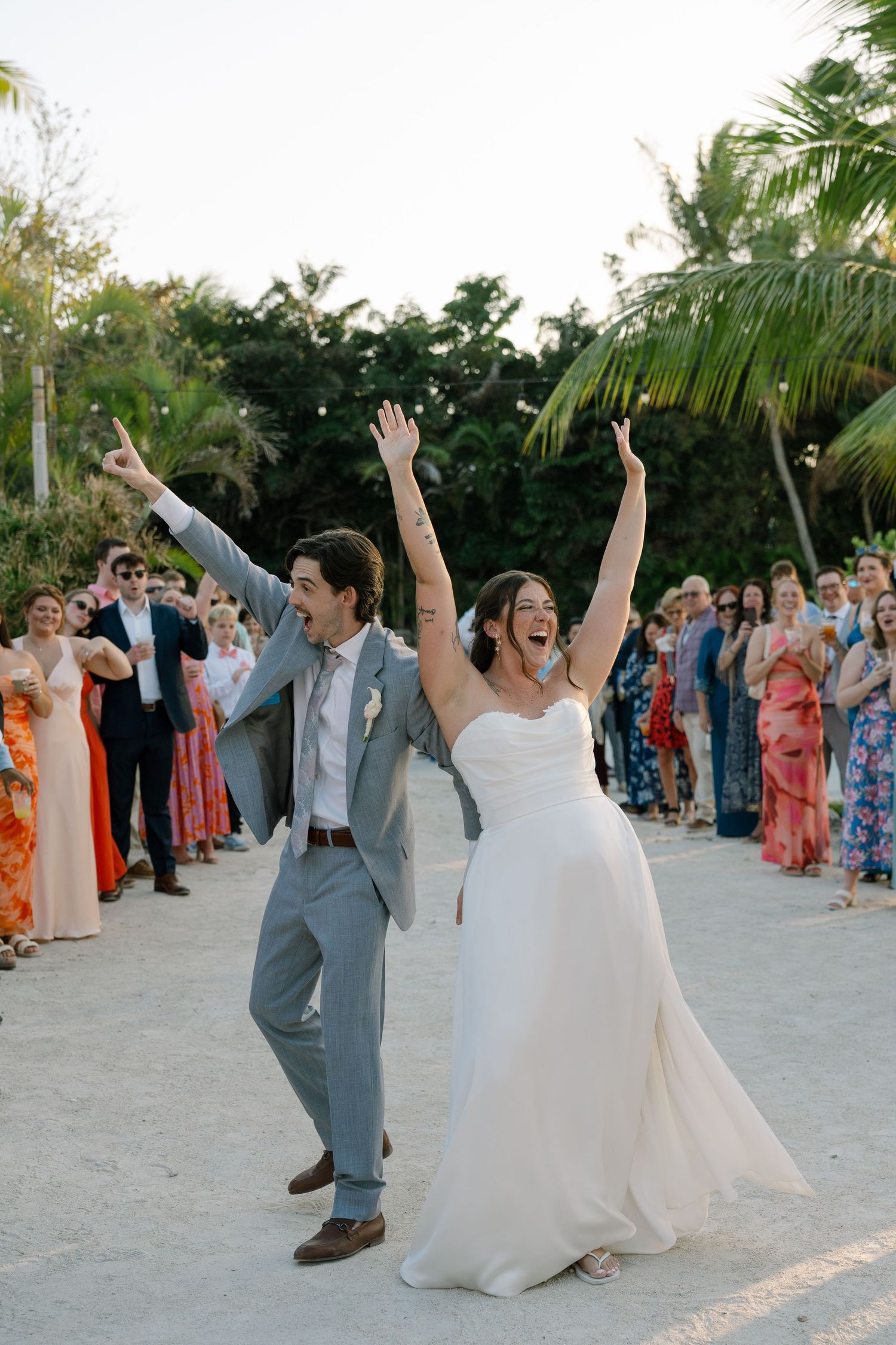 A bride and groom joyfully celebrating their wedding, with their guests cheering and raising their arms.