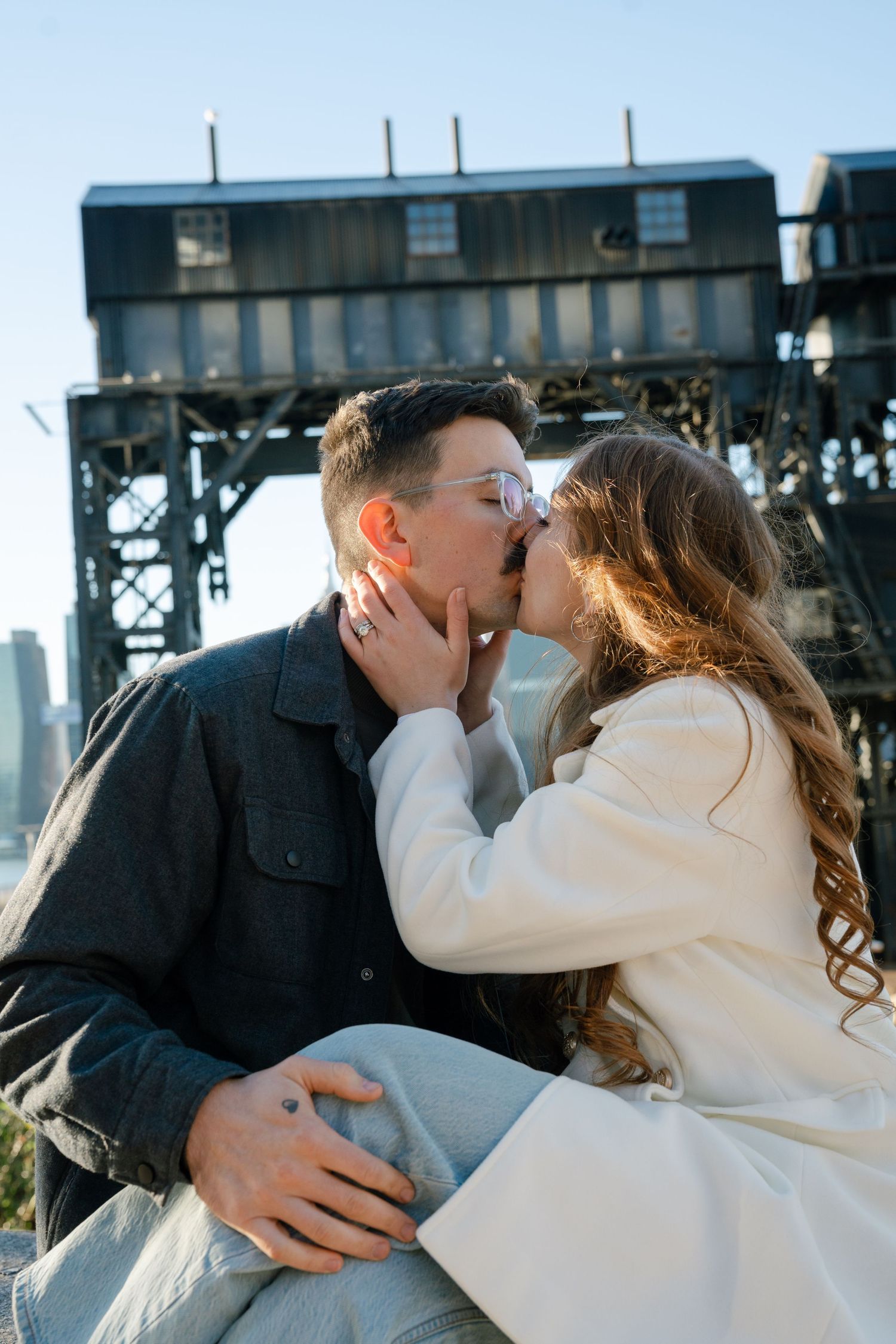 A romantic couple shares intimate kisses against an industrial waterfront backdrop.