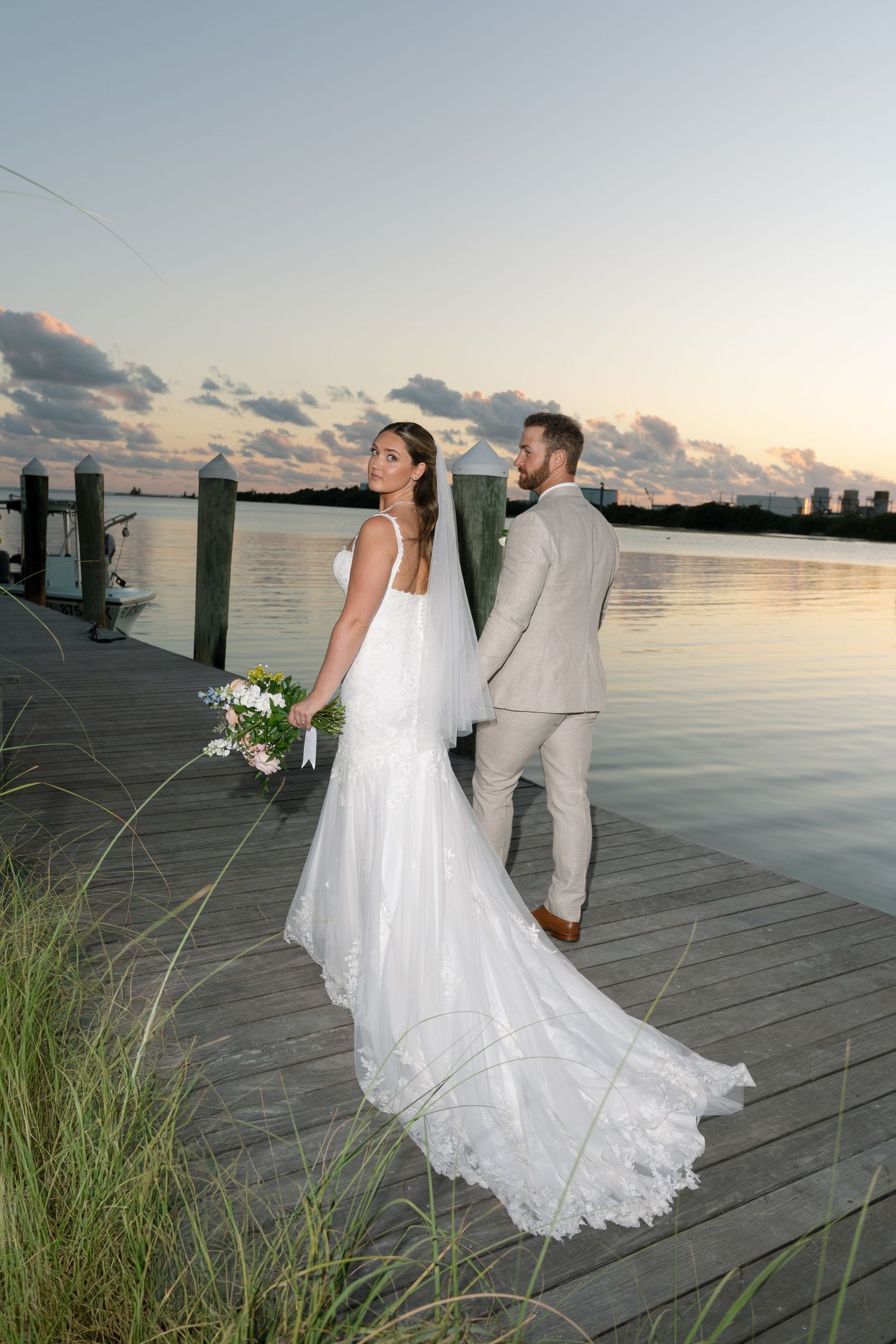 Newlyweds pose for romantic sunset photos on a wooden dock by the water.