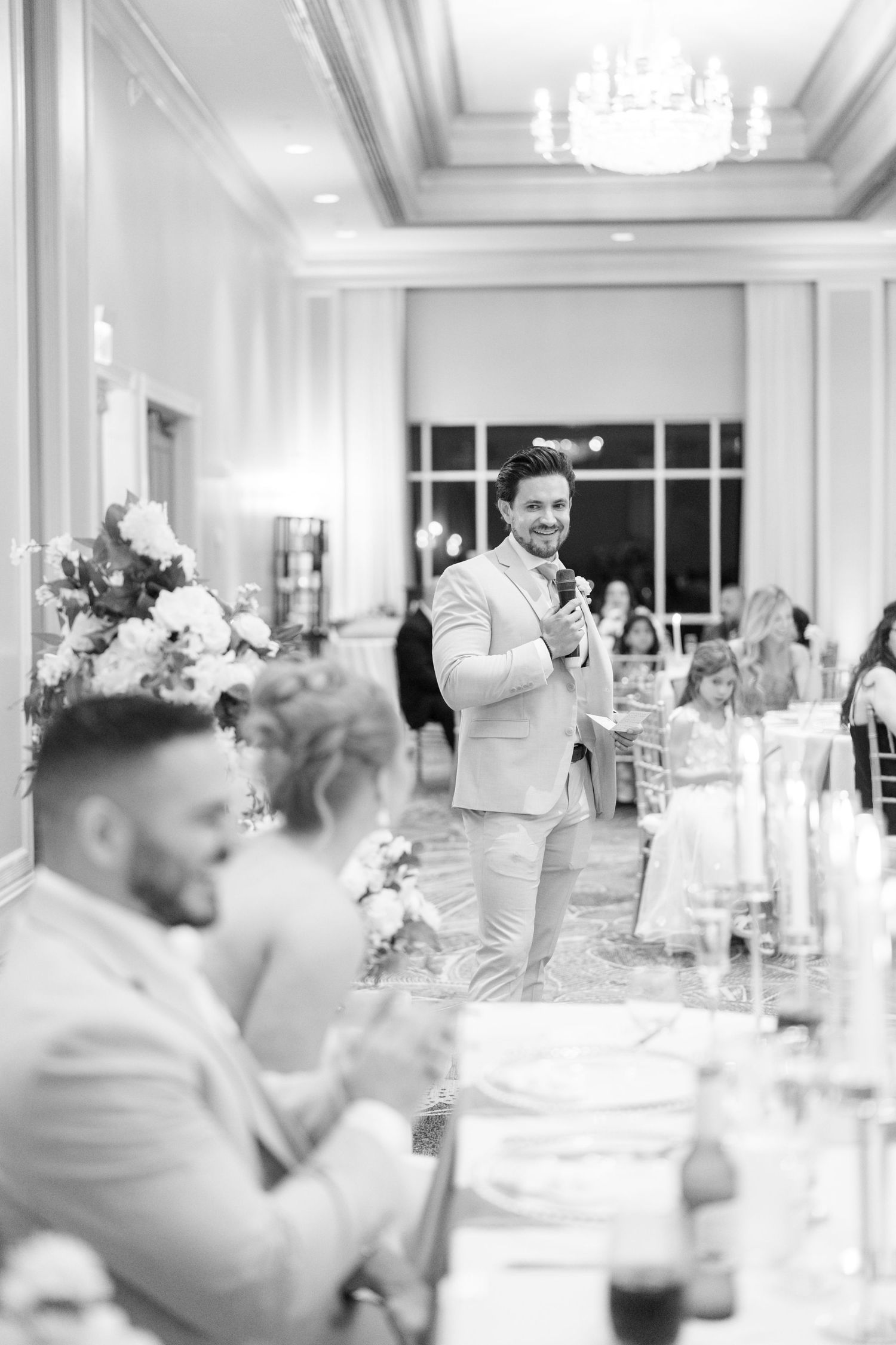 Wedding reception guests raise their glasses in celebration at an elegant white-decorated venue.