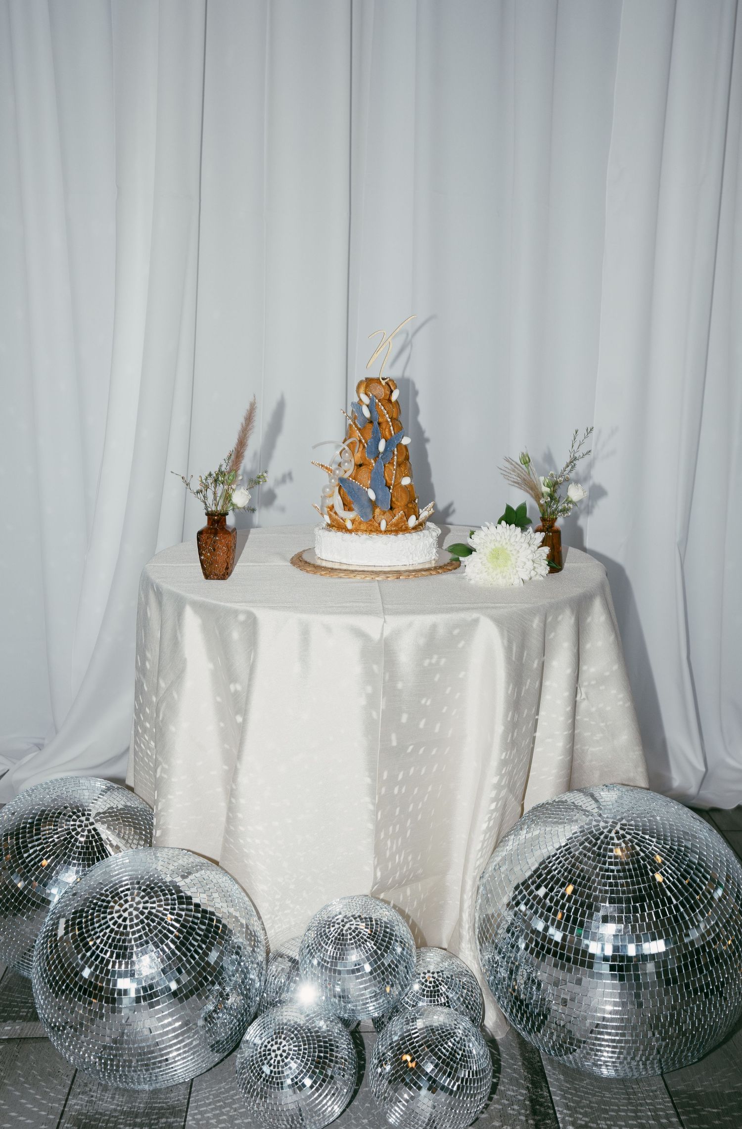 Wedding cake on white tablecloth surrounded by silver disco balls creating a retro dance party atmosphere.