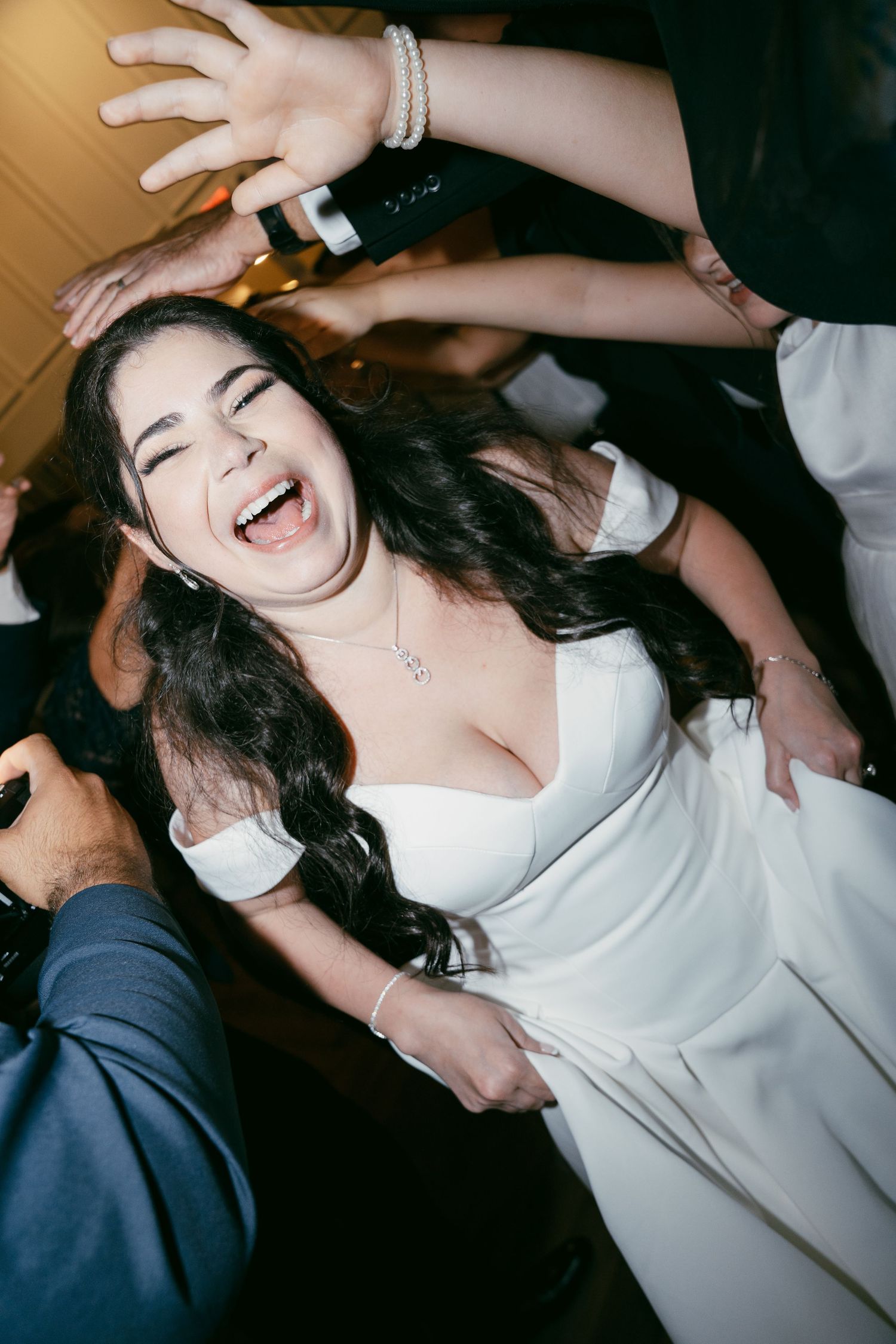 Someone wearing a white dress and pearl bracelet laughs joyfully while dancing at what appears to be a celebration party.