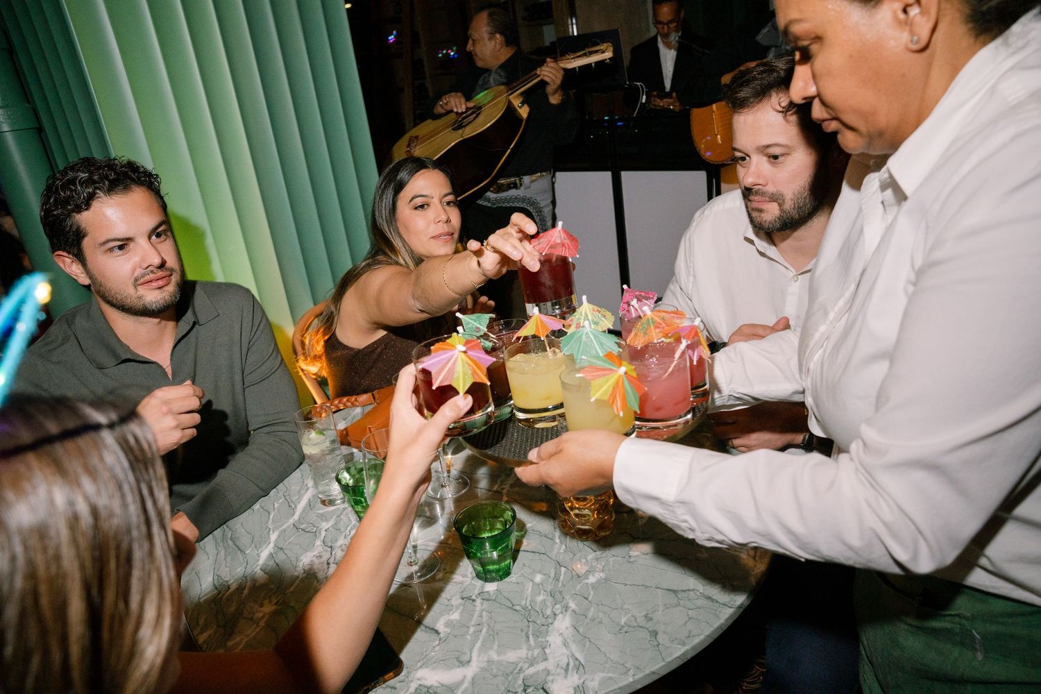 Party guests enjoying drinks and conversation at a dimly lit evening celebration.