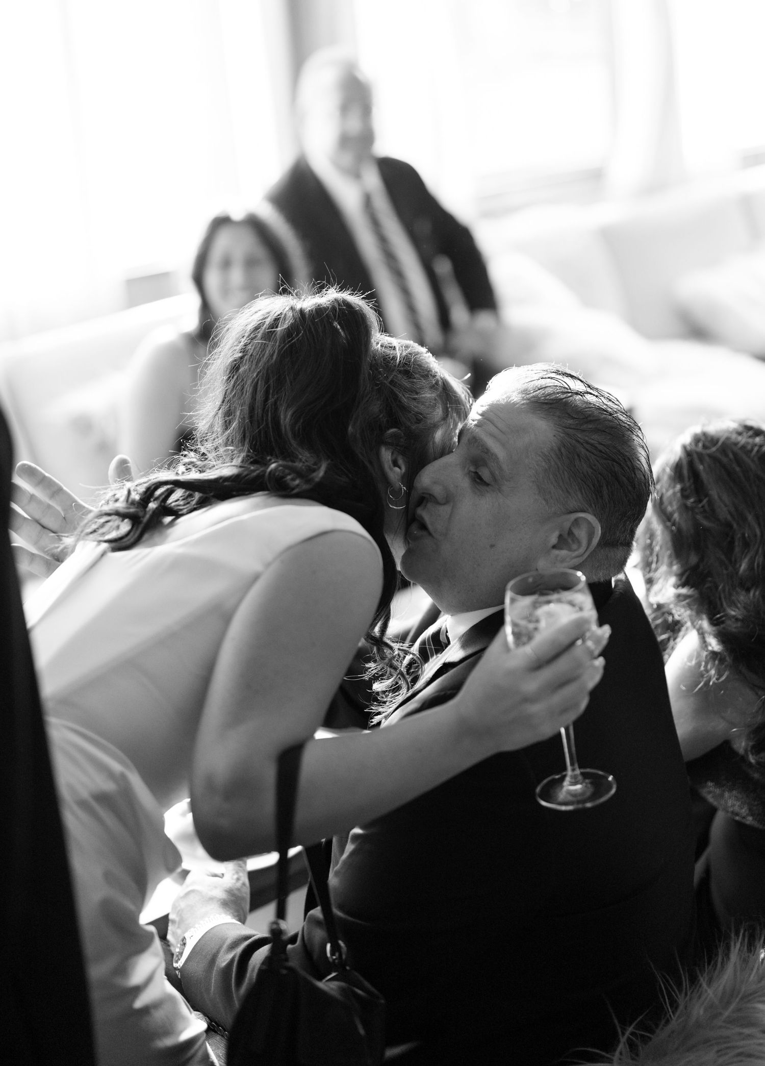 Black and white candid photo of wedding guests embracing in an emotional moment.