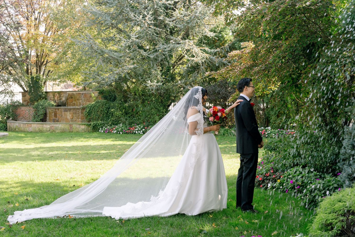 A wedding couple walks through a lush garden path surrounded by blooming trees and greenery on their special day.