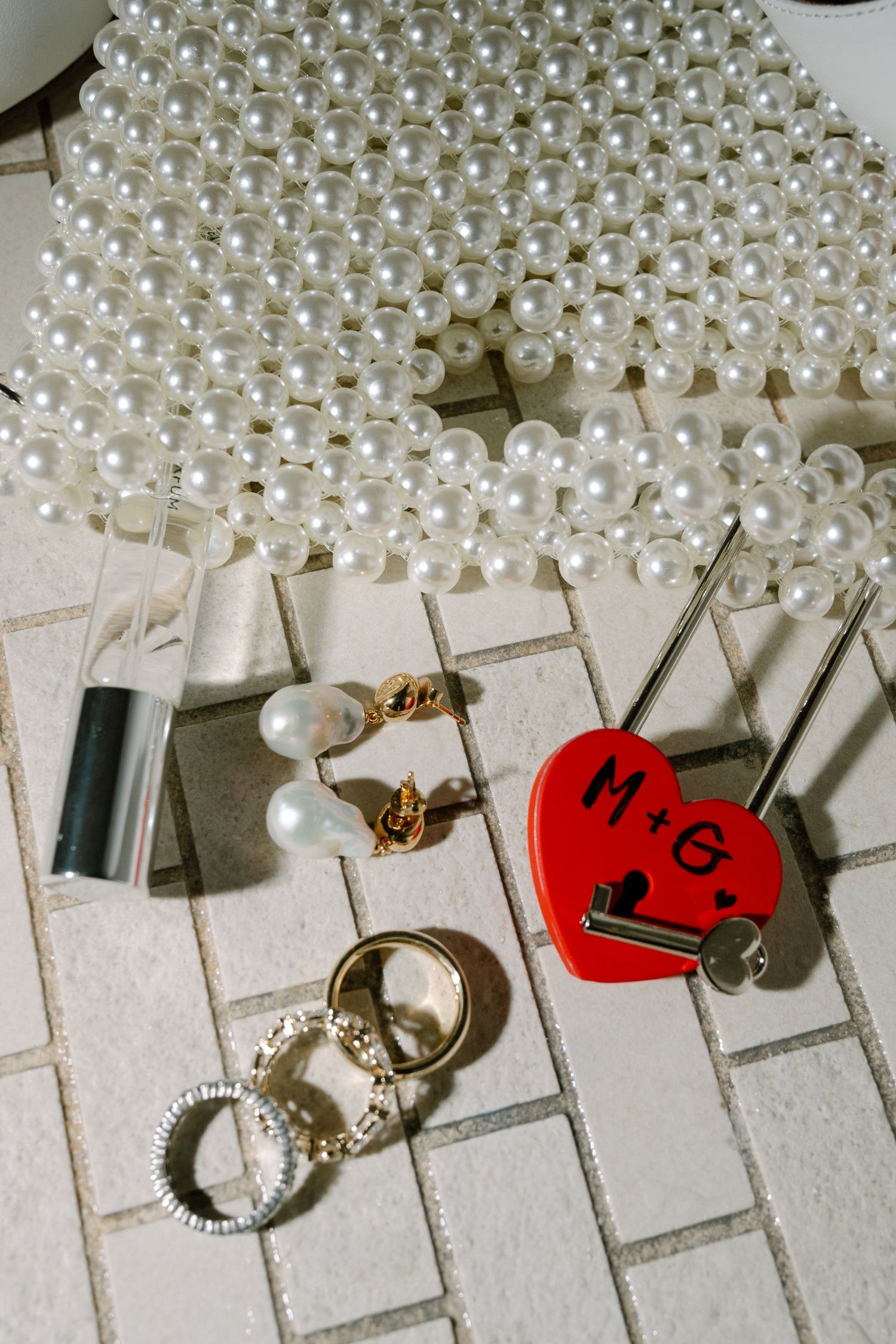 Pearl beaded necklace displayed with jewelry and accessories including rings, earrings and a red key tag on a white surface.