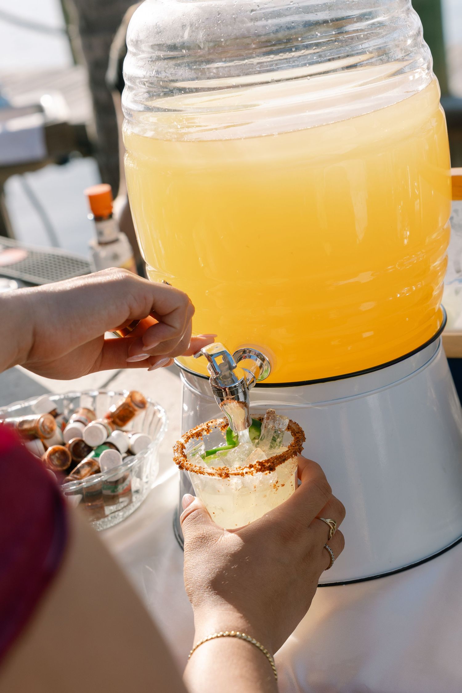 A person's hands hold a glass of orange liquid, likely a cocktail or juice, in front of a blurred background.