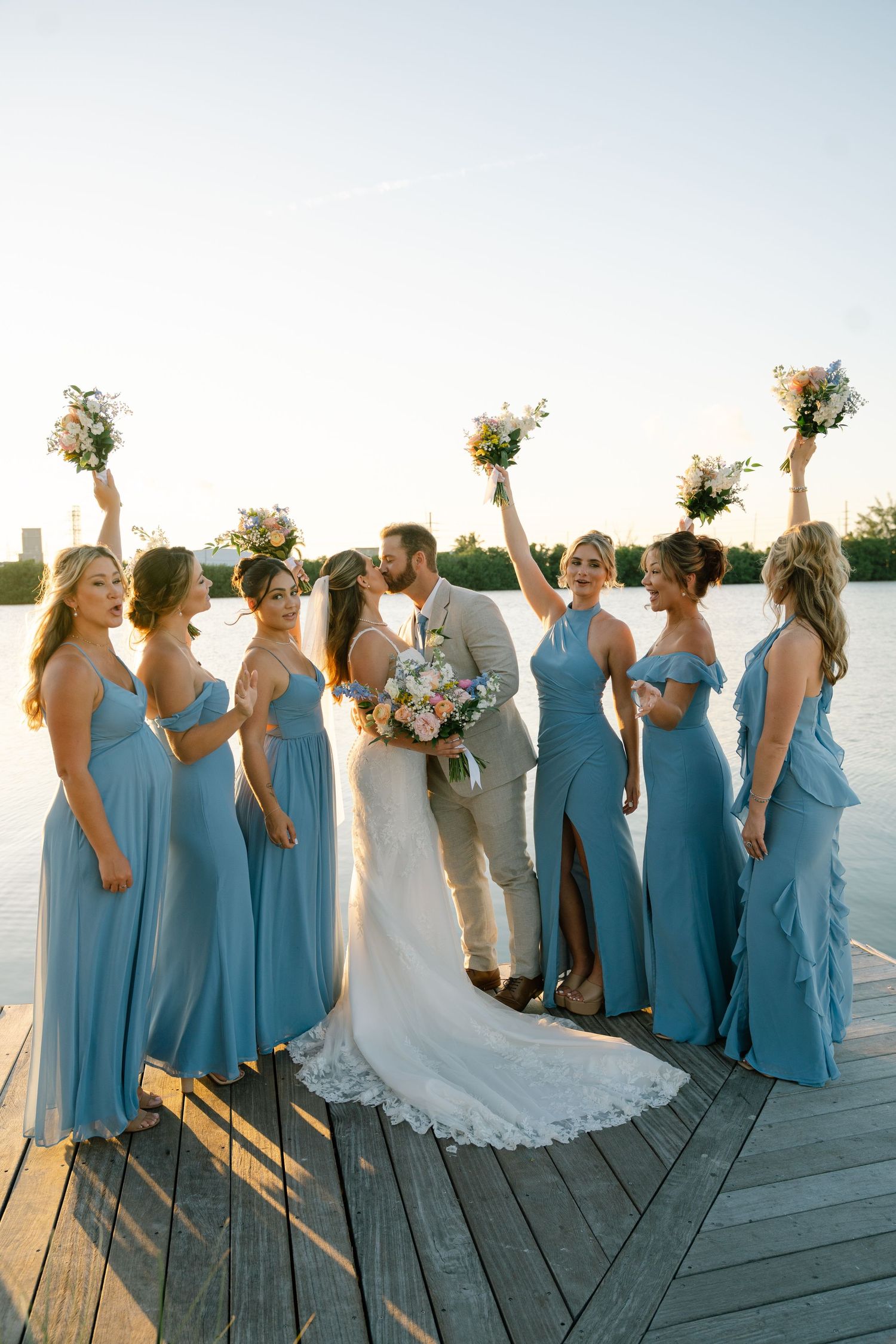 Wedding party poses playfully on wooden dock with bridesmaids in matching blue dresses.