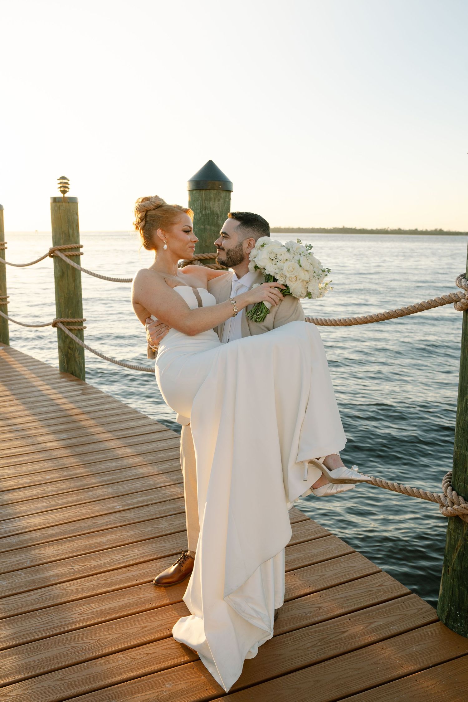 Newlyweds share romantic moments on a waterfront dock during golden hour.