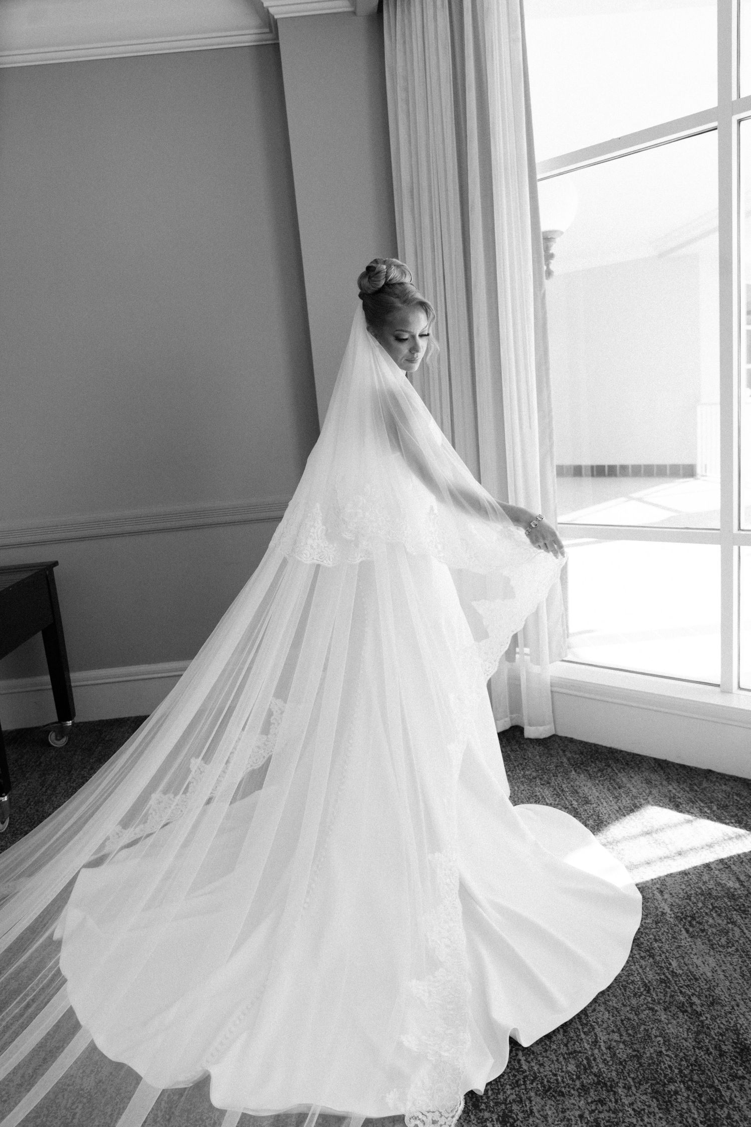 A flowing white wedding dress with a dramatic long train and veil photographed in a bright sunlit room.