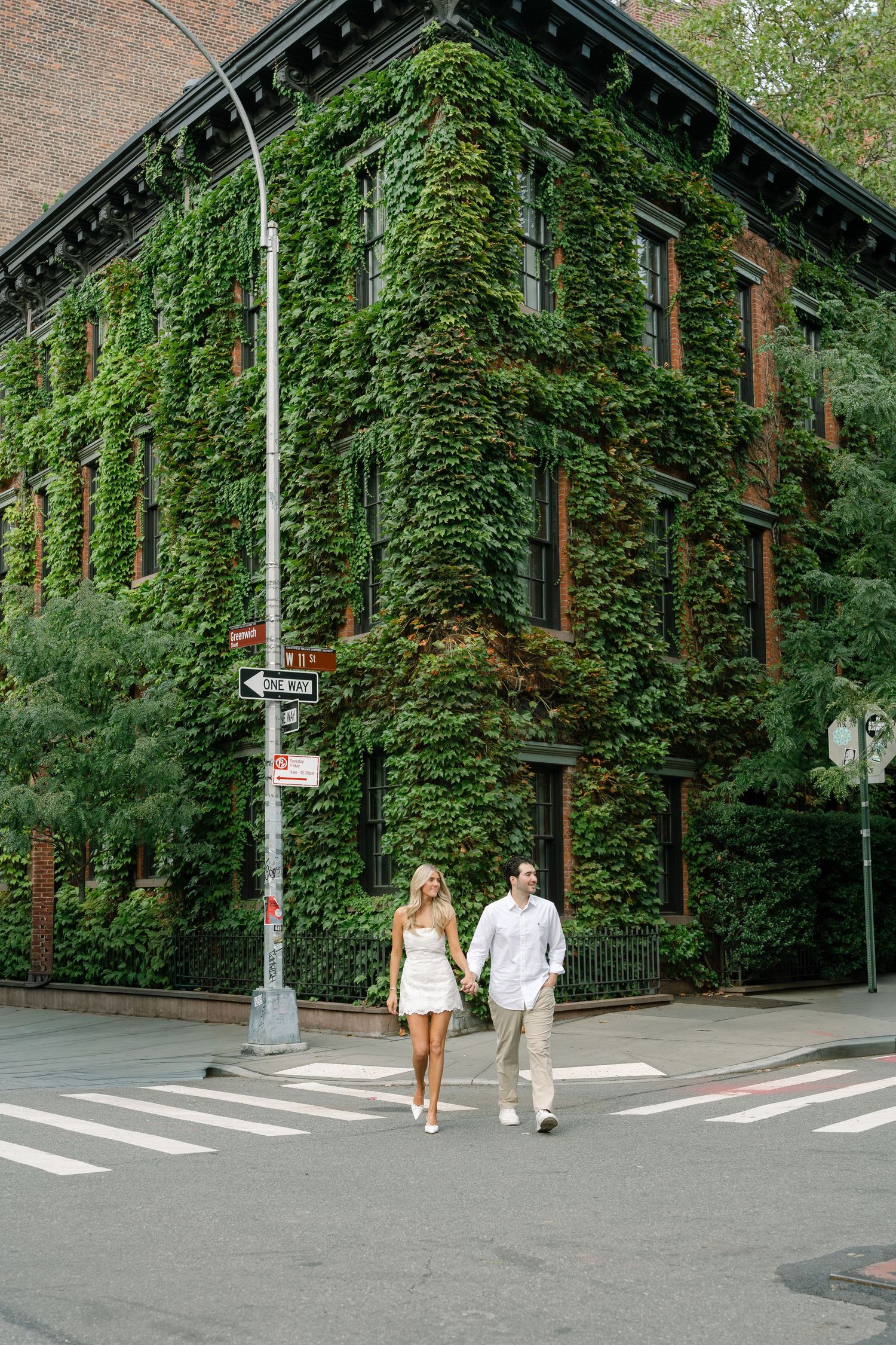 Couple holding hands crossing a street in front of an ivy-covered brick building in New York City.