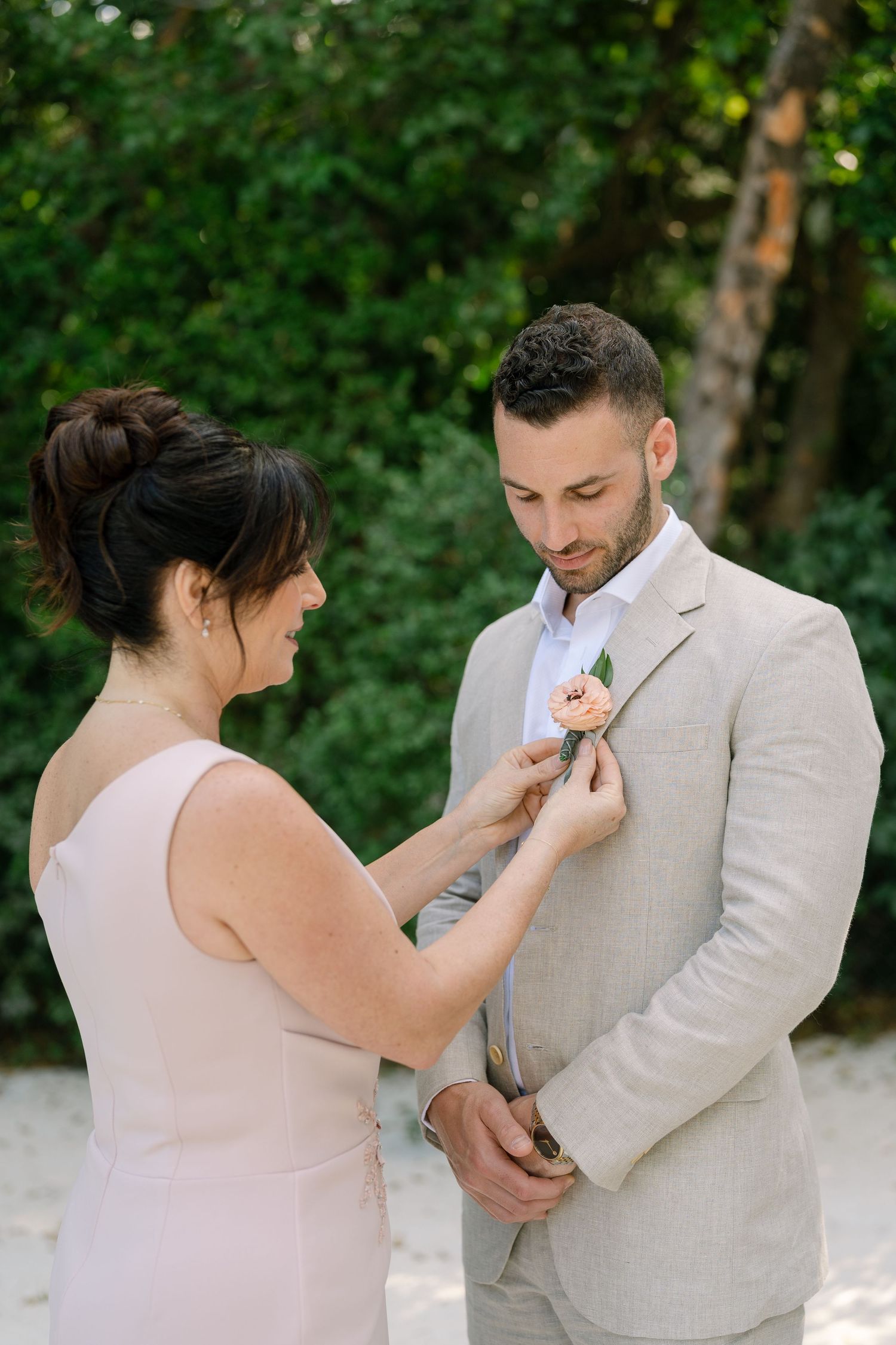Wedding couple adjusting boutonnieres and details of their attire in an outdoor garden setting.