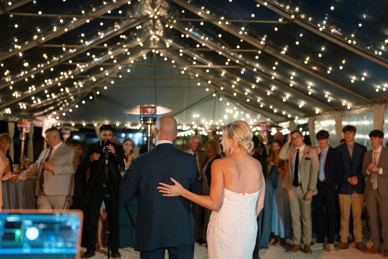 Couple dancing under twinkling lights at an evening wedding reception.