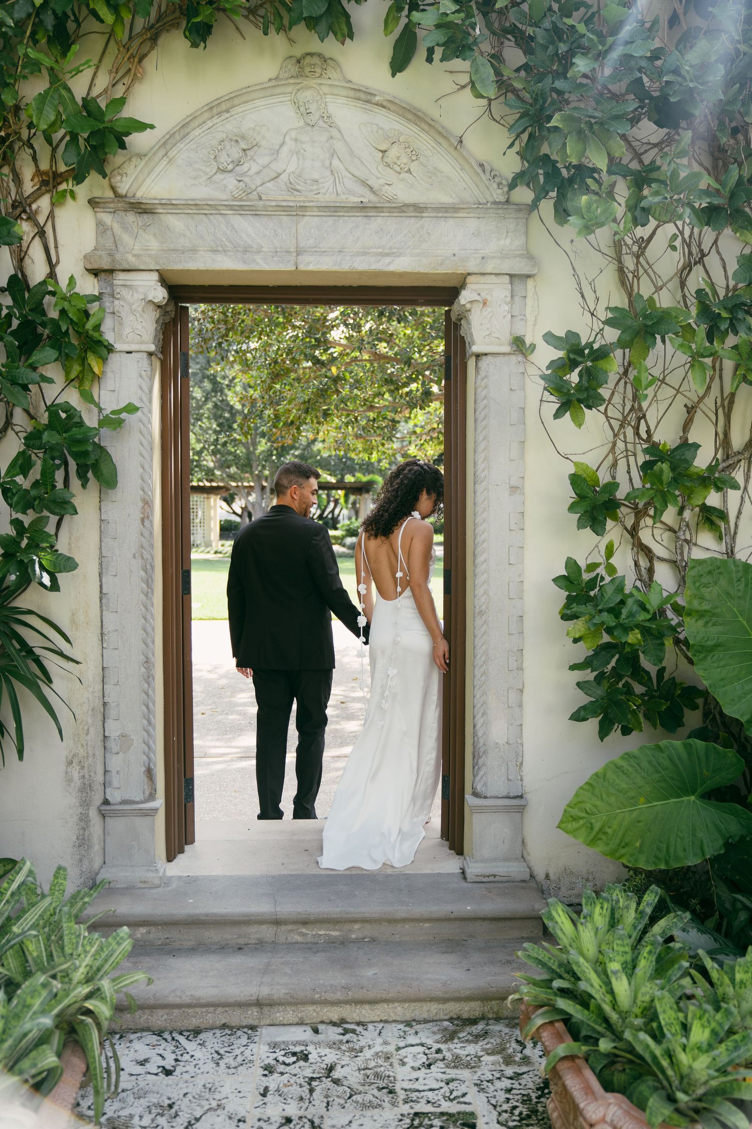 Stone archway framed with lush green vines and foliage in a romantic garden setting, leading to a sunlit path beyond.