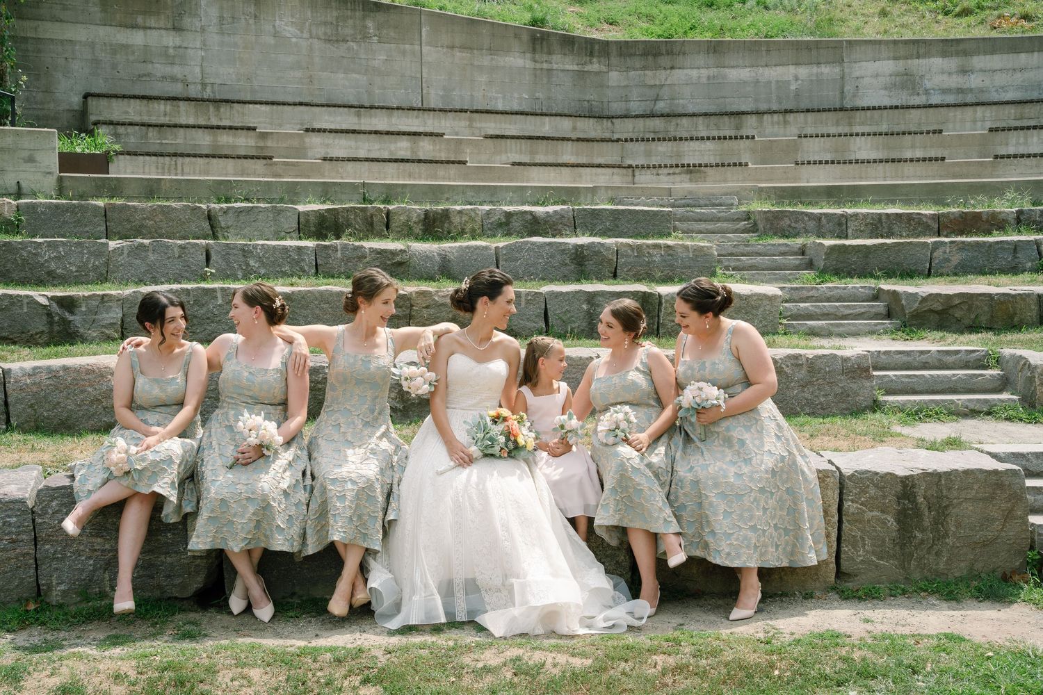 A group in white dresses sits casually on stone amphitheater steps while chatting and relaxing outdoors.