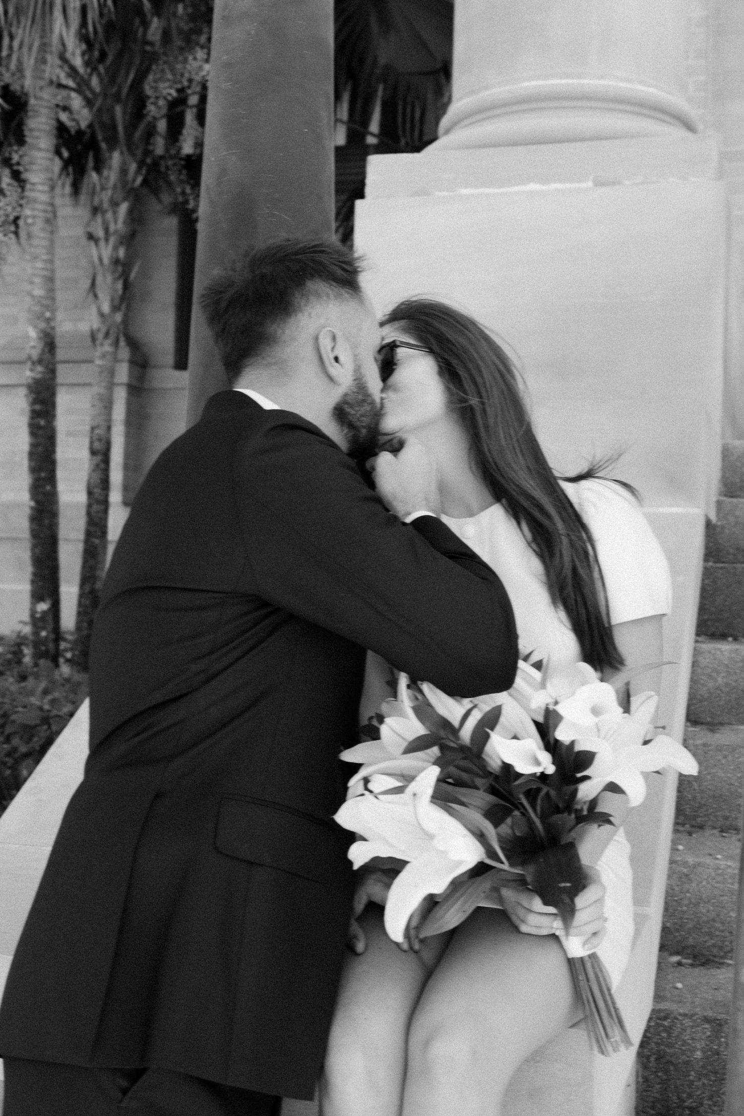 A couple embraces during their wedding ceremony with white lilies in hand.