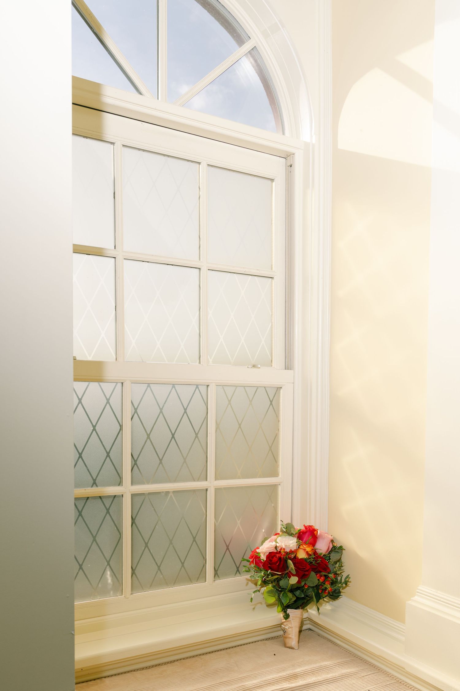 Elegant white interior room with diamond-paned windows and red floral arrangements.