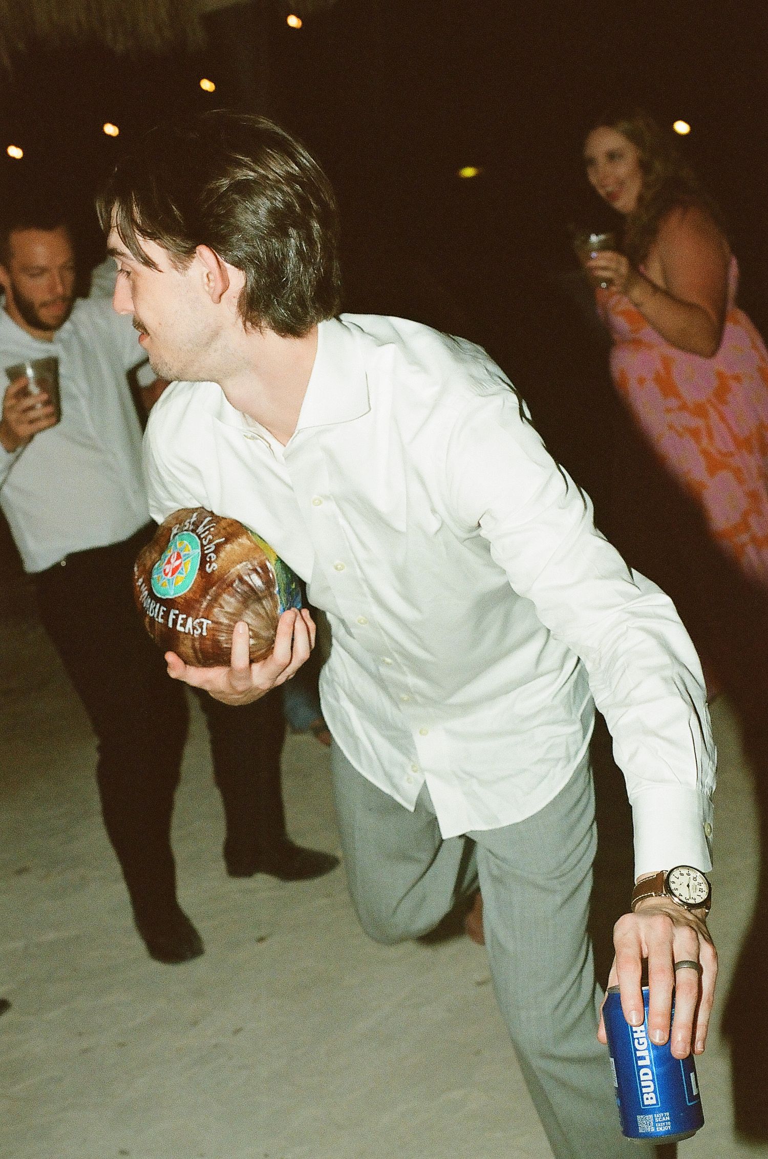 A man in a white shirt and jeans dancing with a drink in his hand at a party.