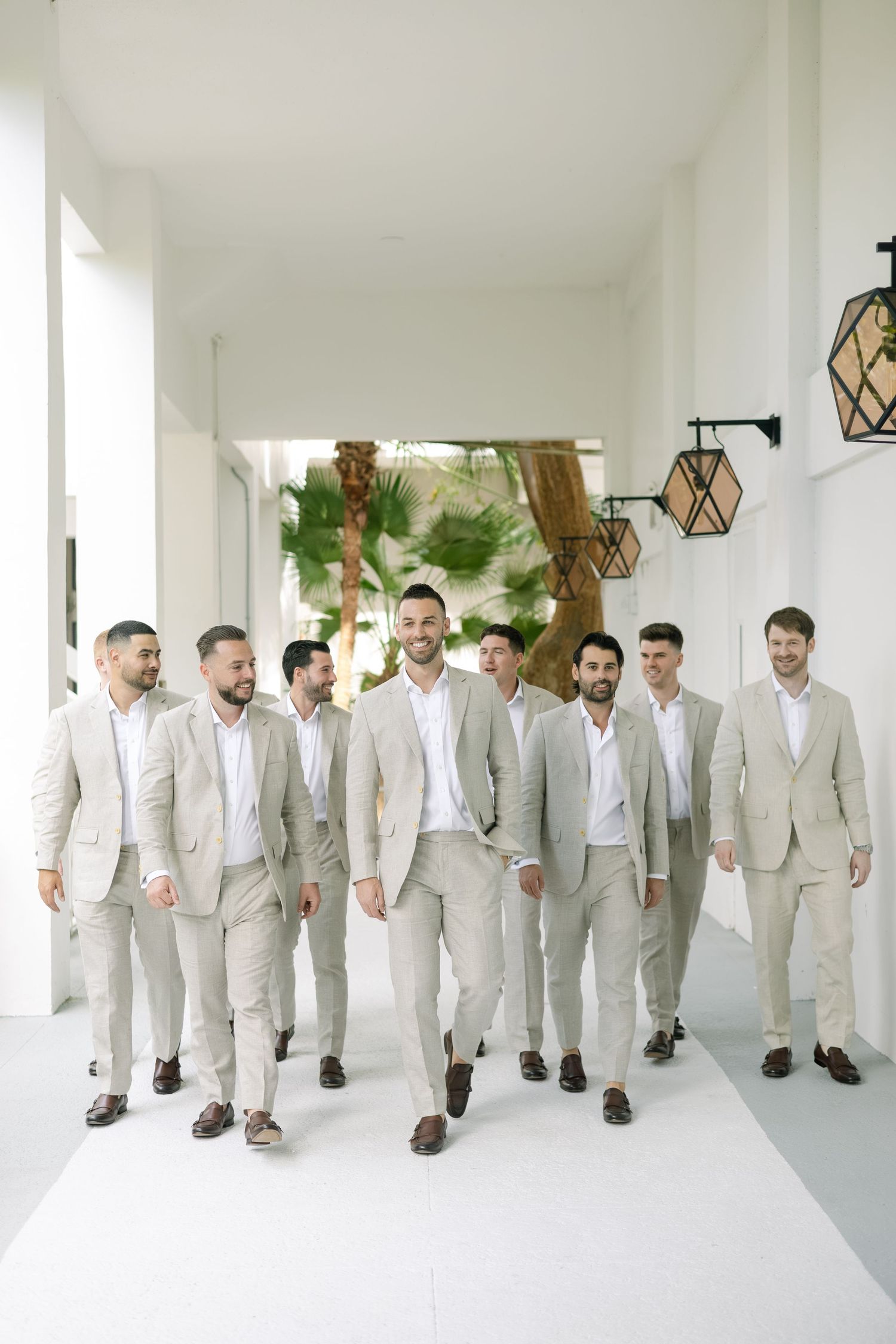 Groomsmen in light gray suits walking together in a modern white interior space.