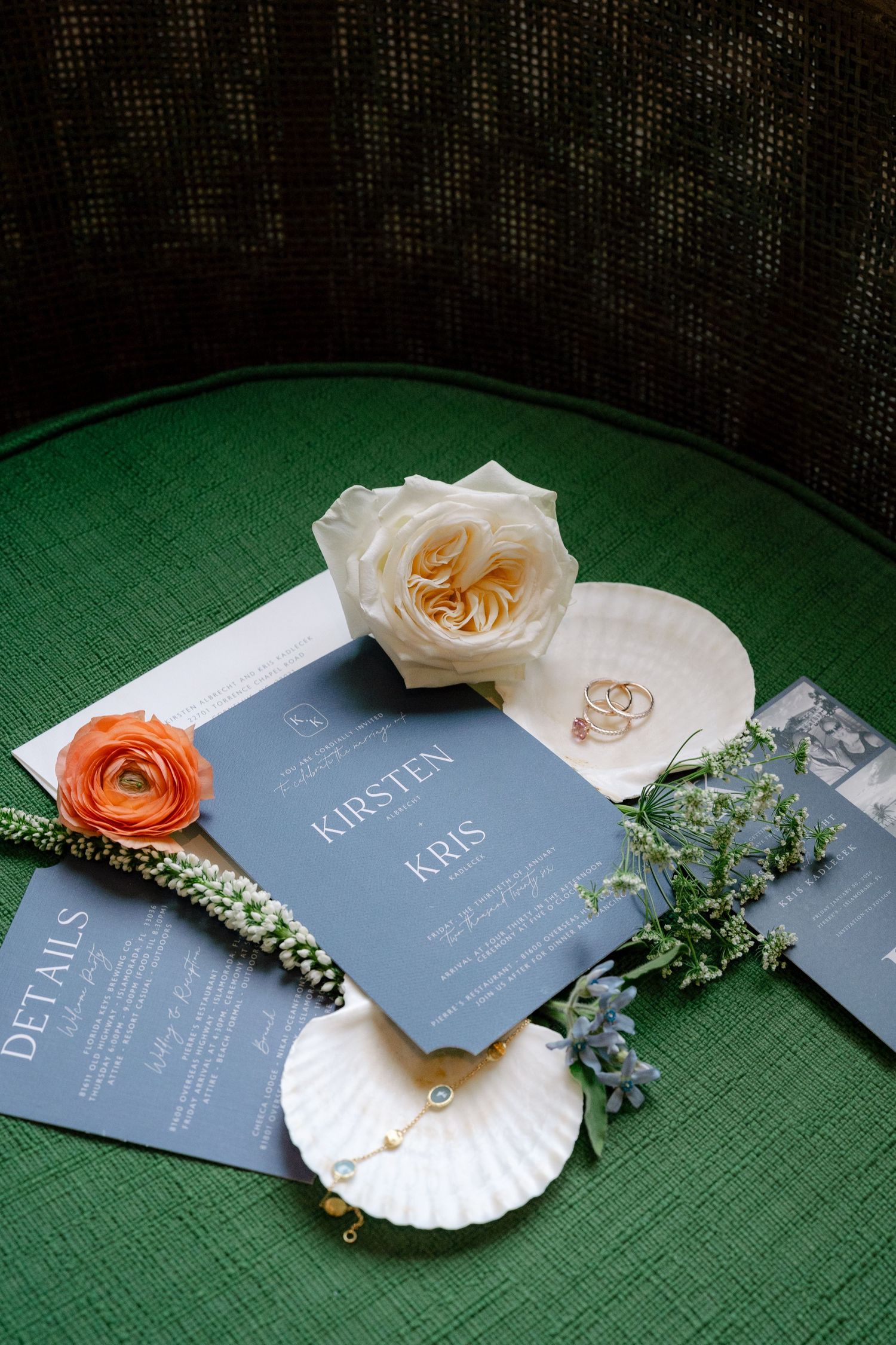 Wedding invitations displayed on green fabric with delicate roses and seashell decorations.