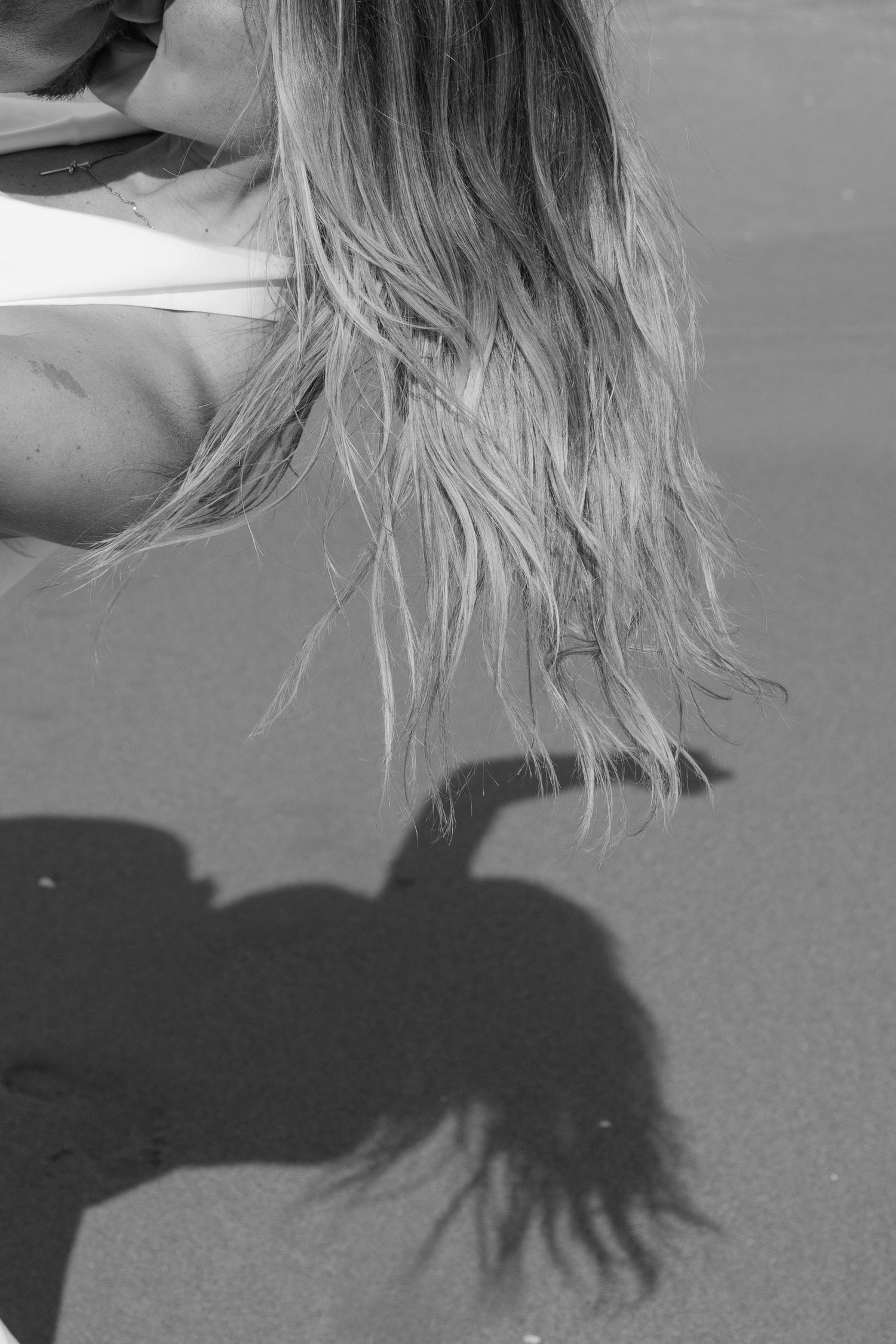 Black and white beach photo of blonde bride with flowing hair and shadow on sand.
