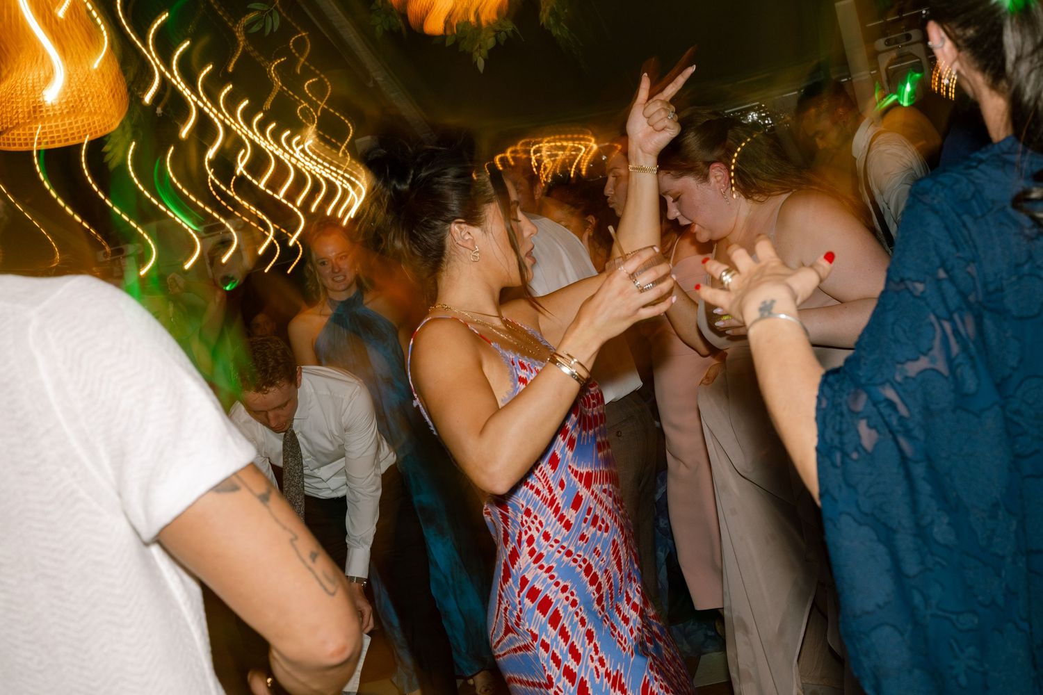 Guests dancing energetically under colorful lights at a lively wedding reception party.
