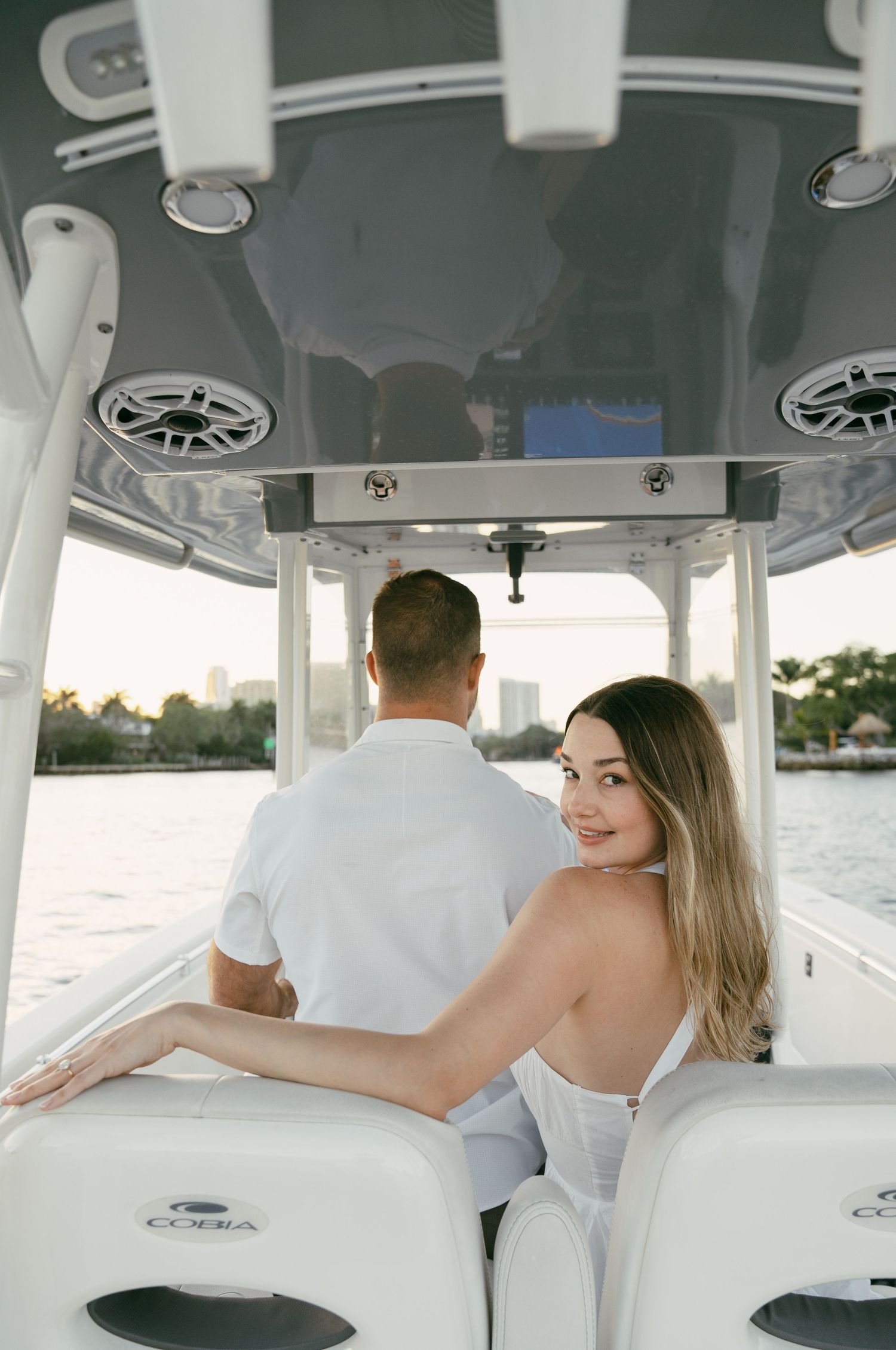 Interior view of a luxury boat cabin showing white leather seating and overhead speakers during a sunny day.