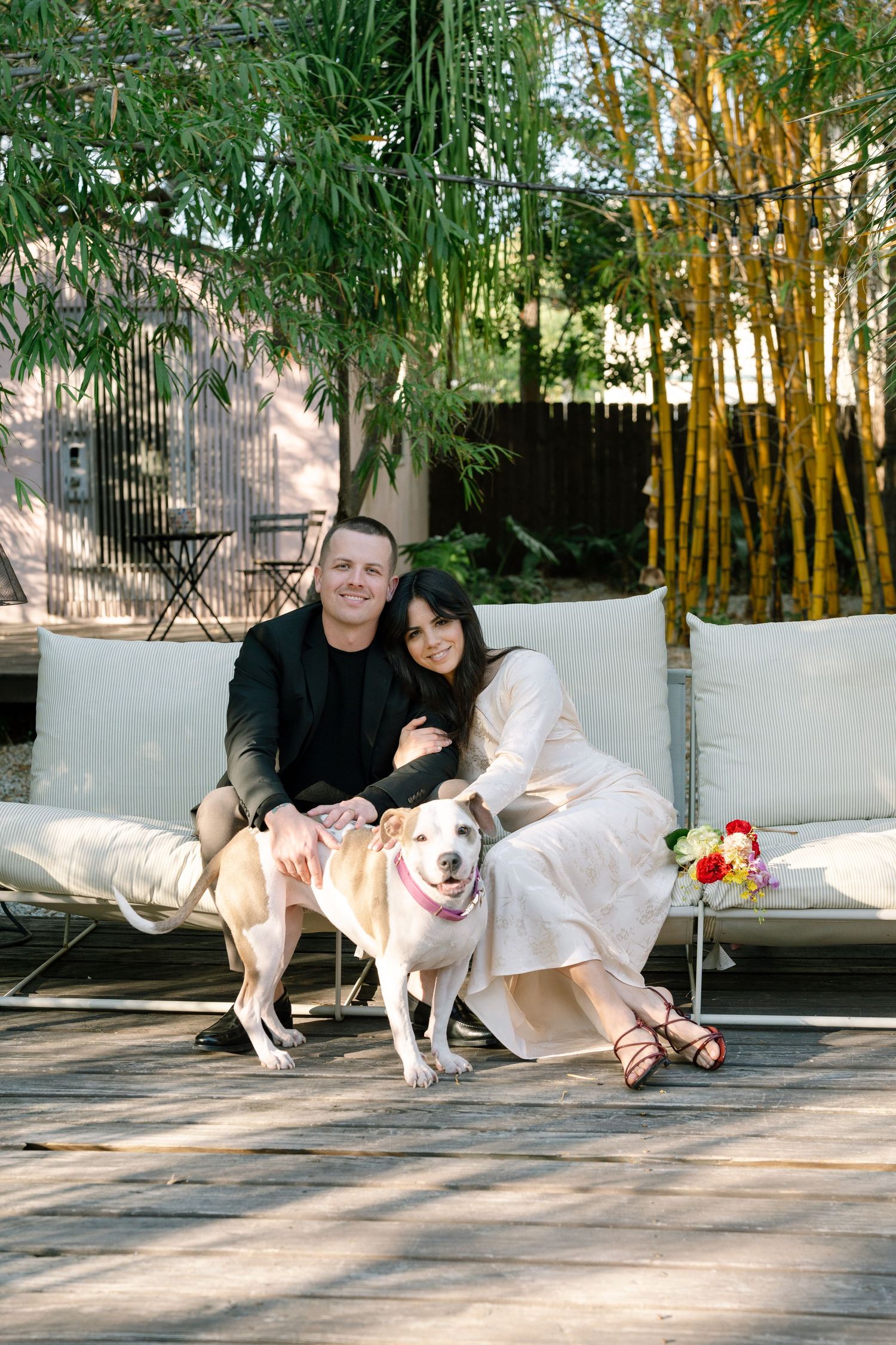 Couple sitting on outdoor patio with white dog in bamboo garden setting.
