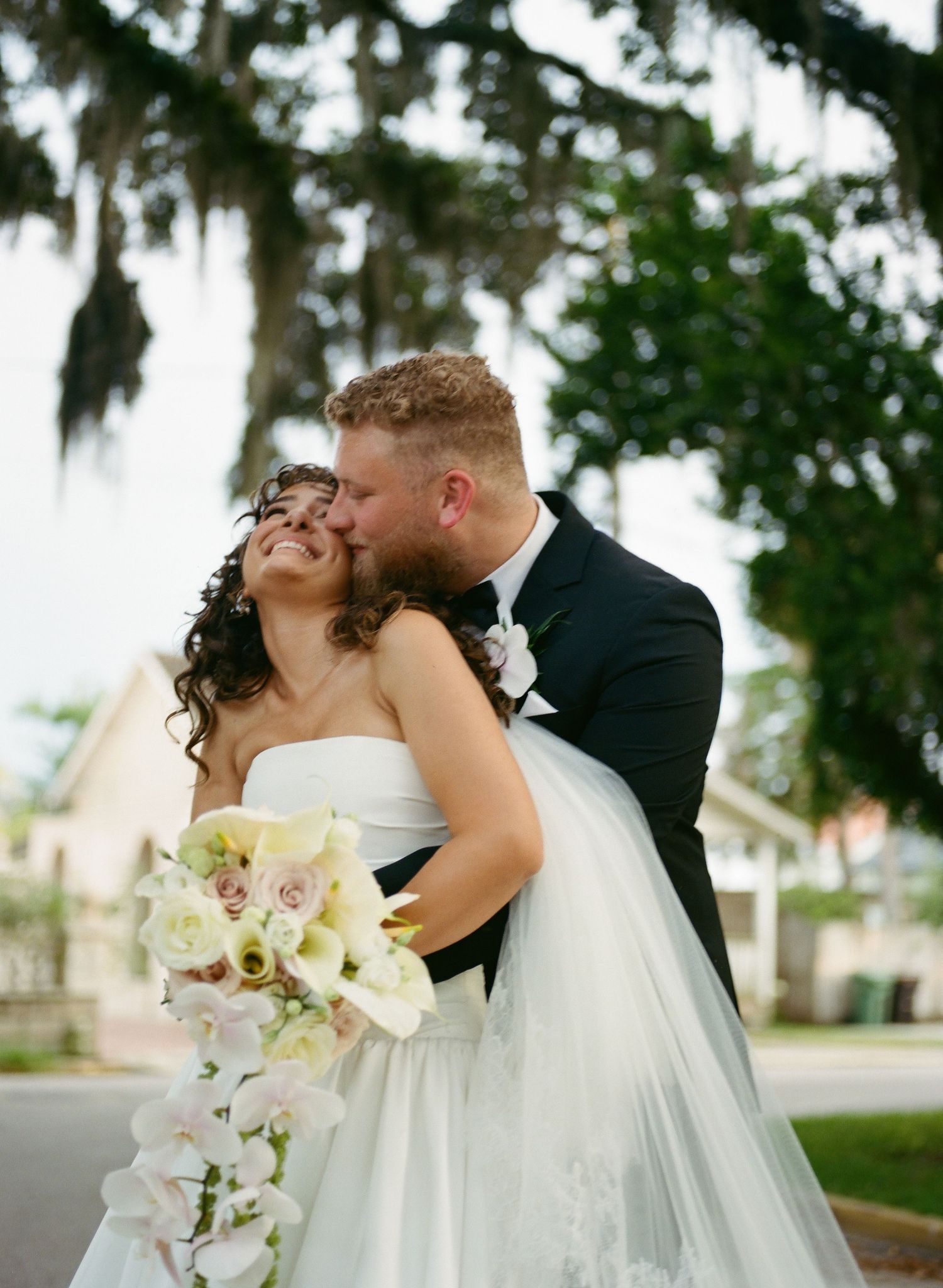 Romantic wedding couple shares intimate moments under Spanish moss draped trees in a garden setting.