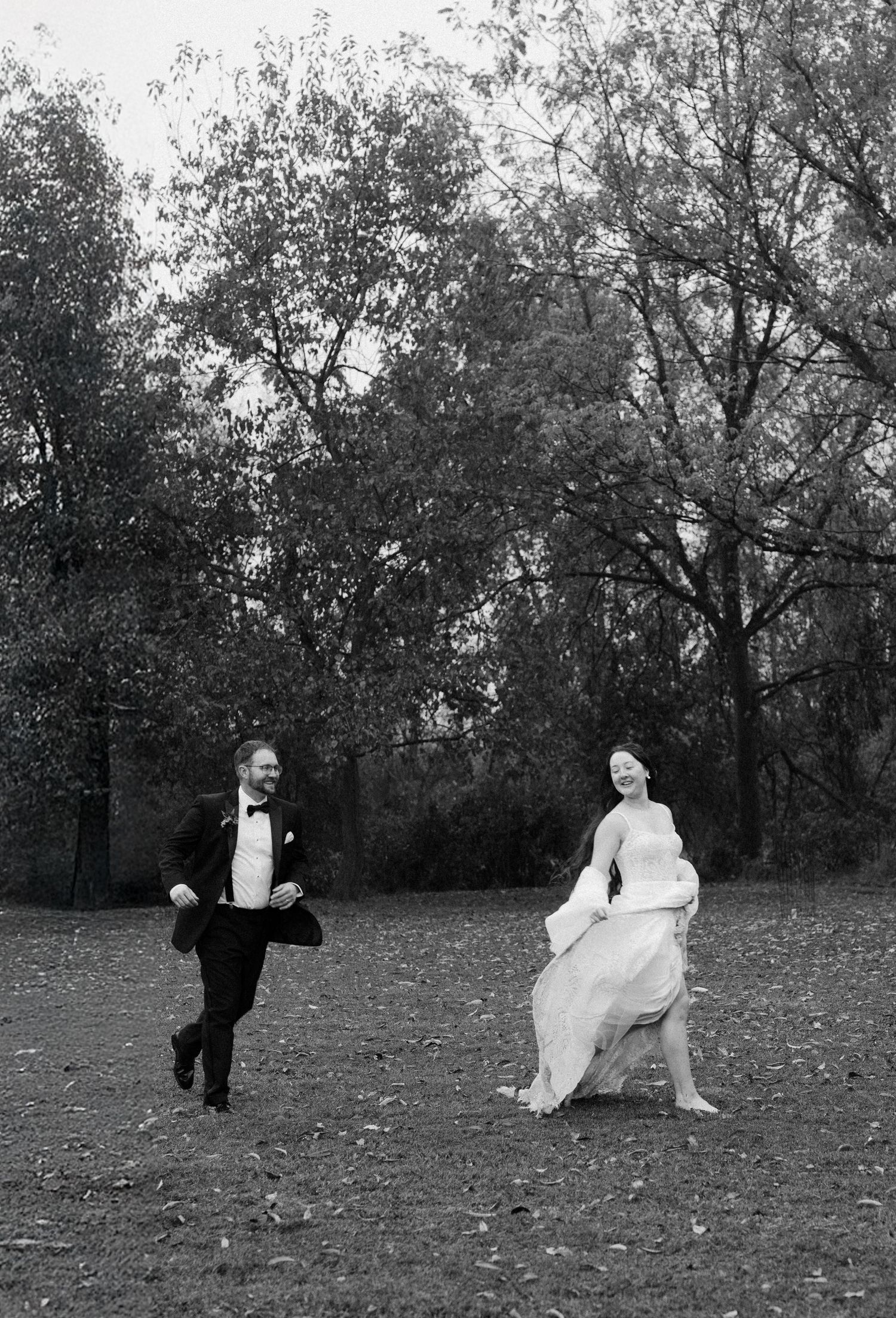 Black and white photo of a couple dancing playfully in a leaf-covered field.